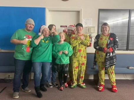 Group of six people wearing holiday pajamas and Christmas sweaters, posing together indoors with smiles.
