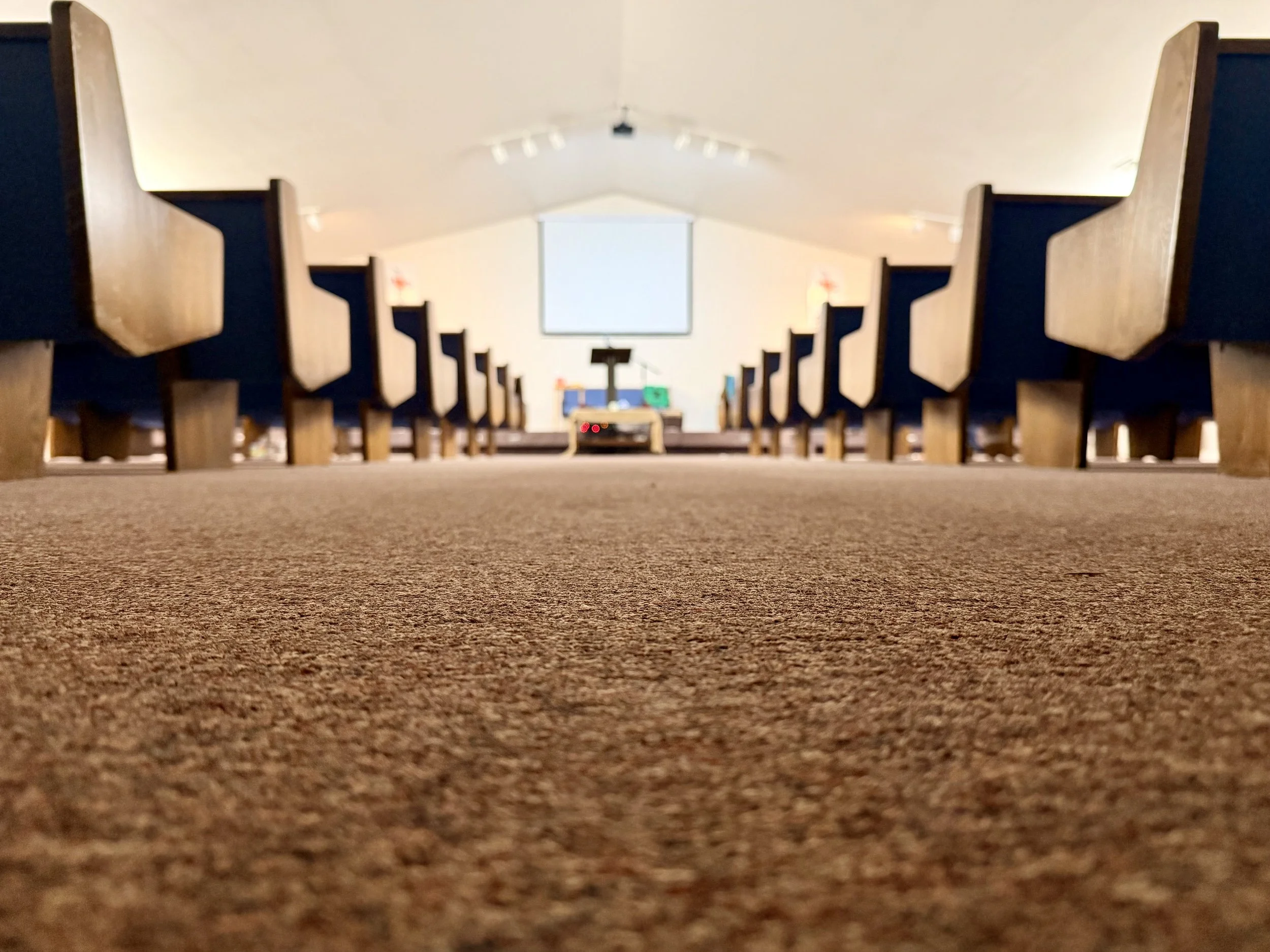 Low-angle view of church pews leading to the altar with a cross, projected onto a screen at the front of the church.