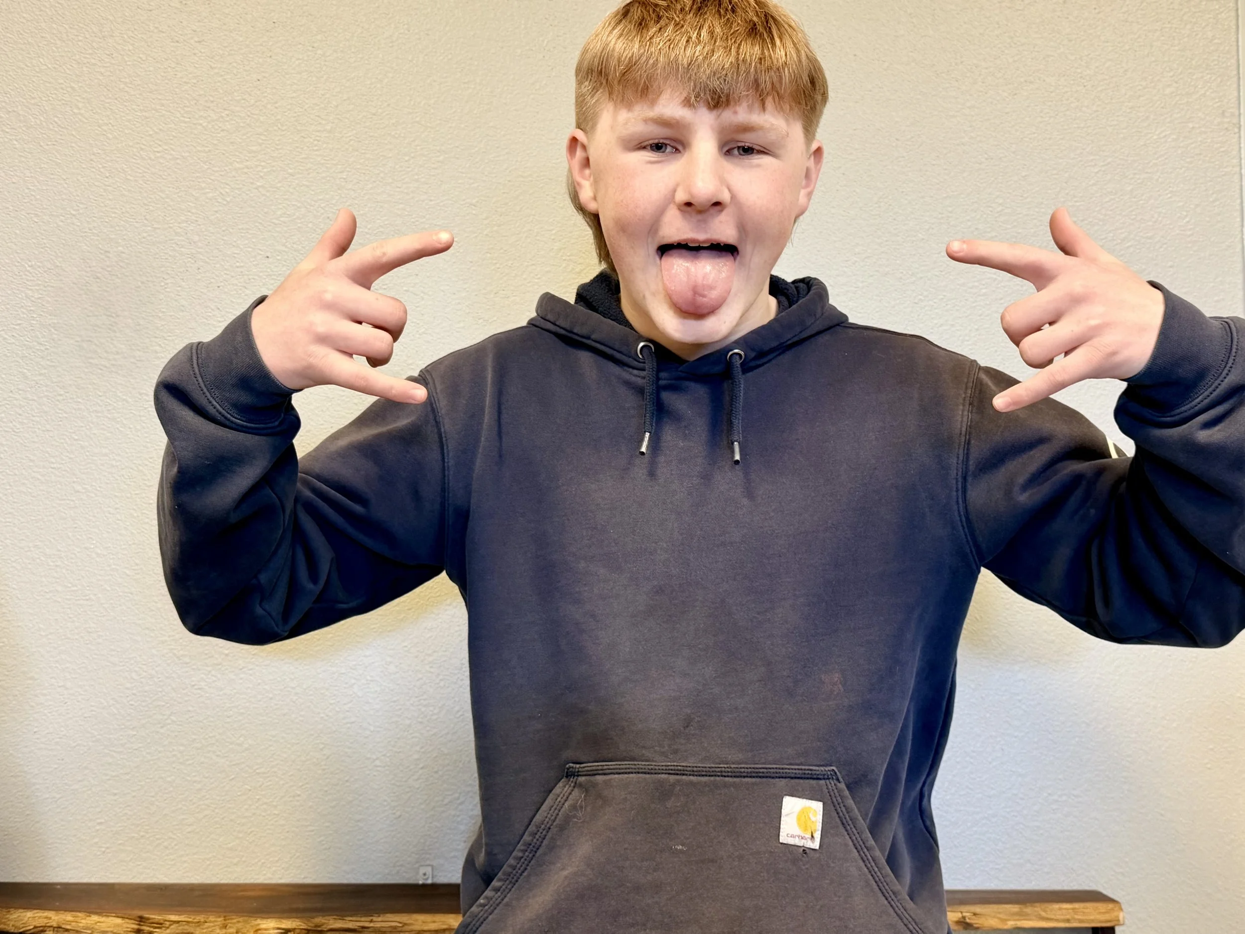 A young man with light skin and red hair sticking out his tongue and making rock and roll hand gestures with both hands.