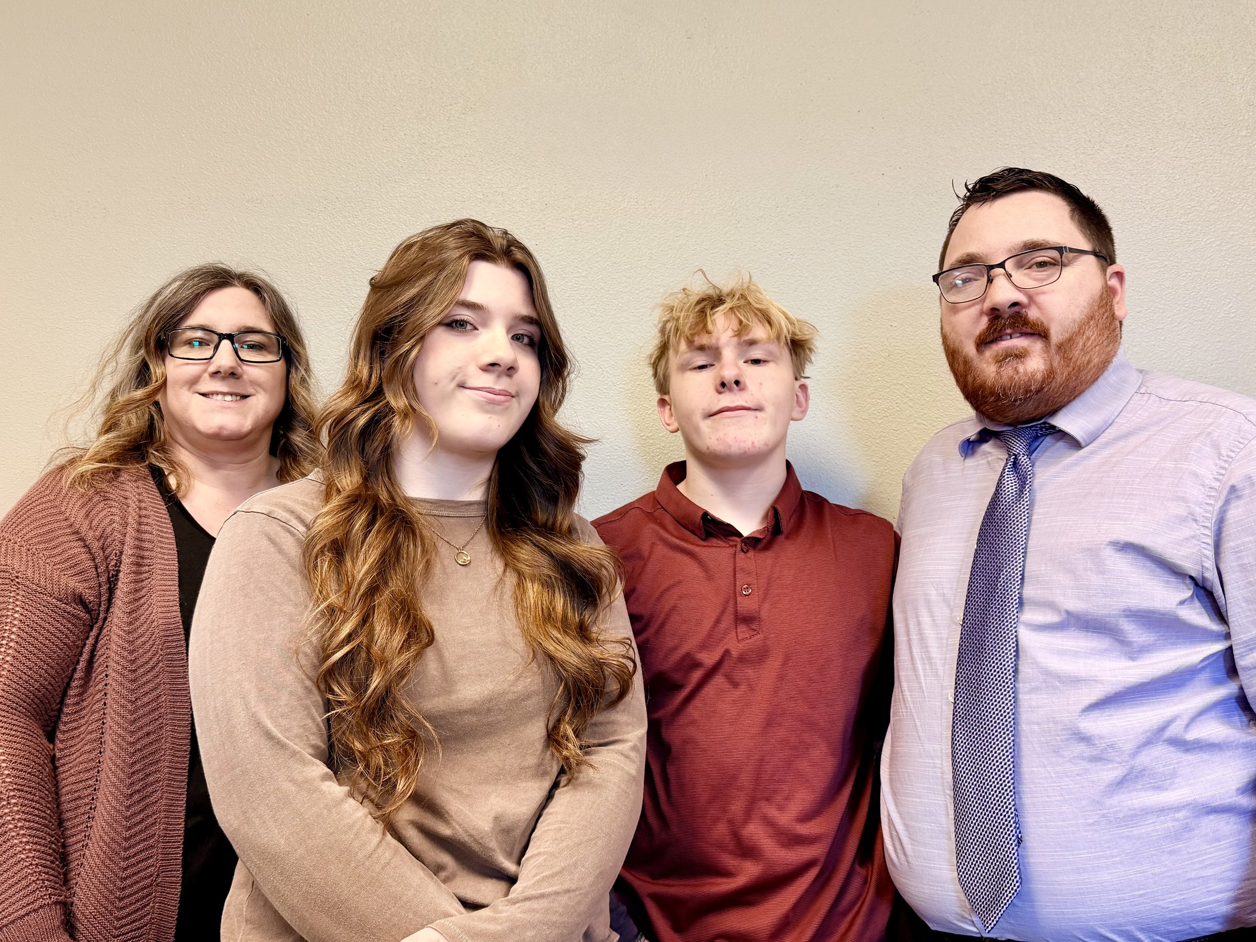 Group of four people, two women and two men, standing close together against a beige wall, smiling for the camera.