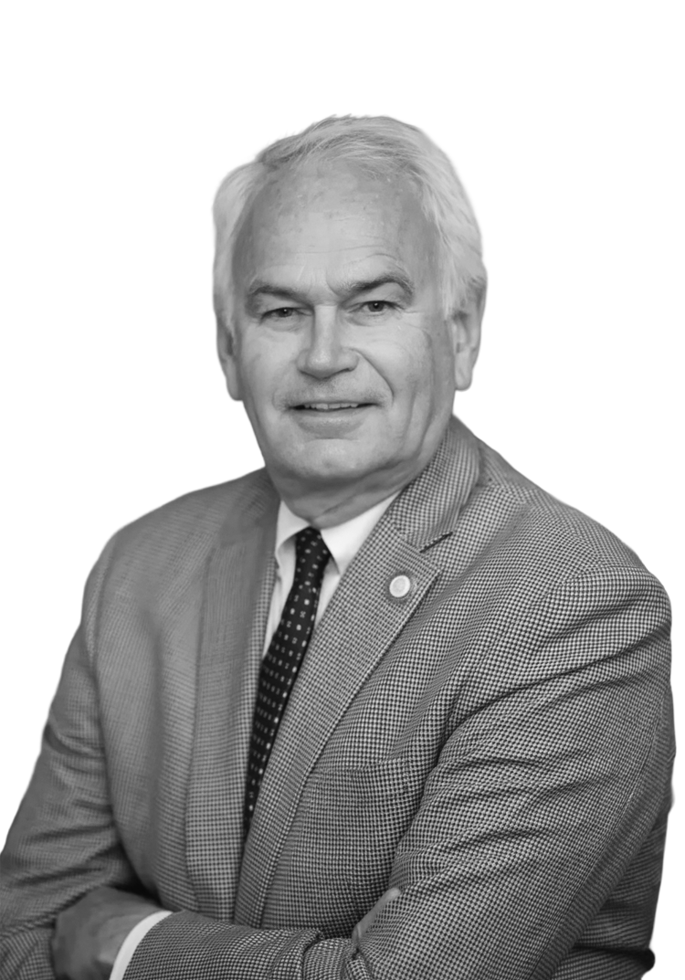 A black and white portrait of an older man with white hair, wearing a suit and tie, looking at the camera with a slight smile.
