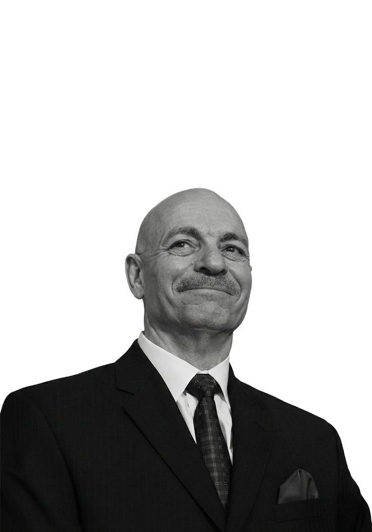 Bald man in a suit and tie with a confident expression, against a black background.