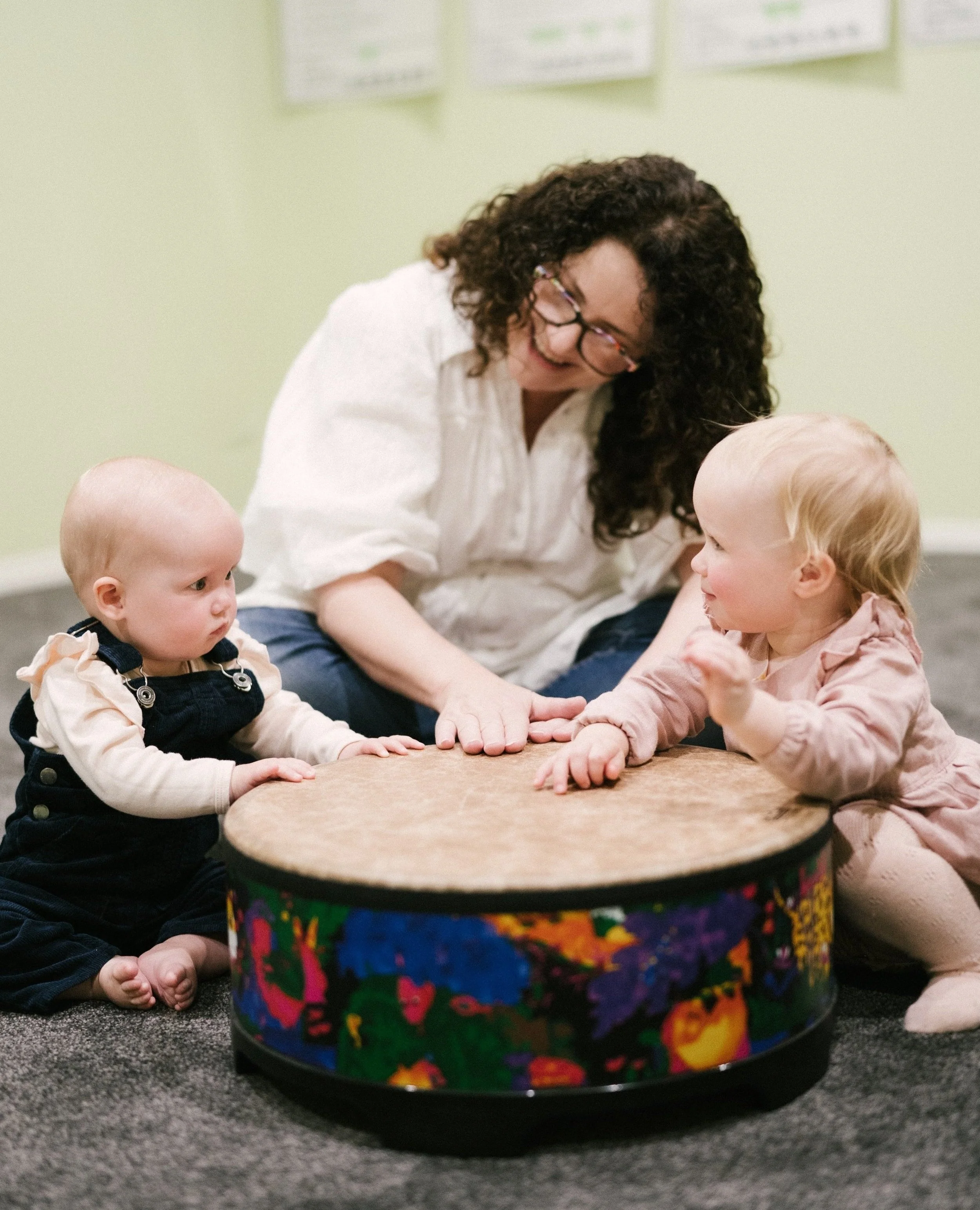 Leisa teaching music to two toddlers, using a colourful drum in her Toowoomba based classroom.