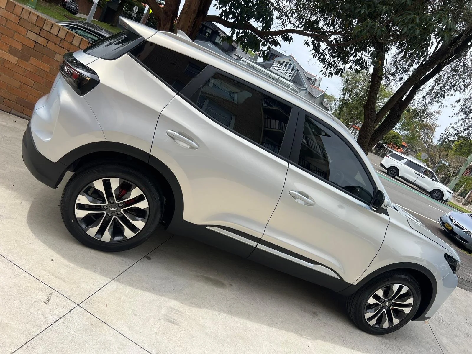 A white SUV parked on a concrete driveway in a residential neighborhood with trees and houses in the background.