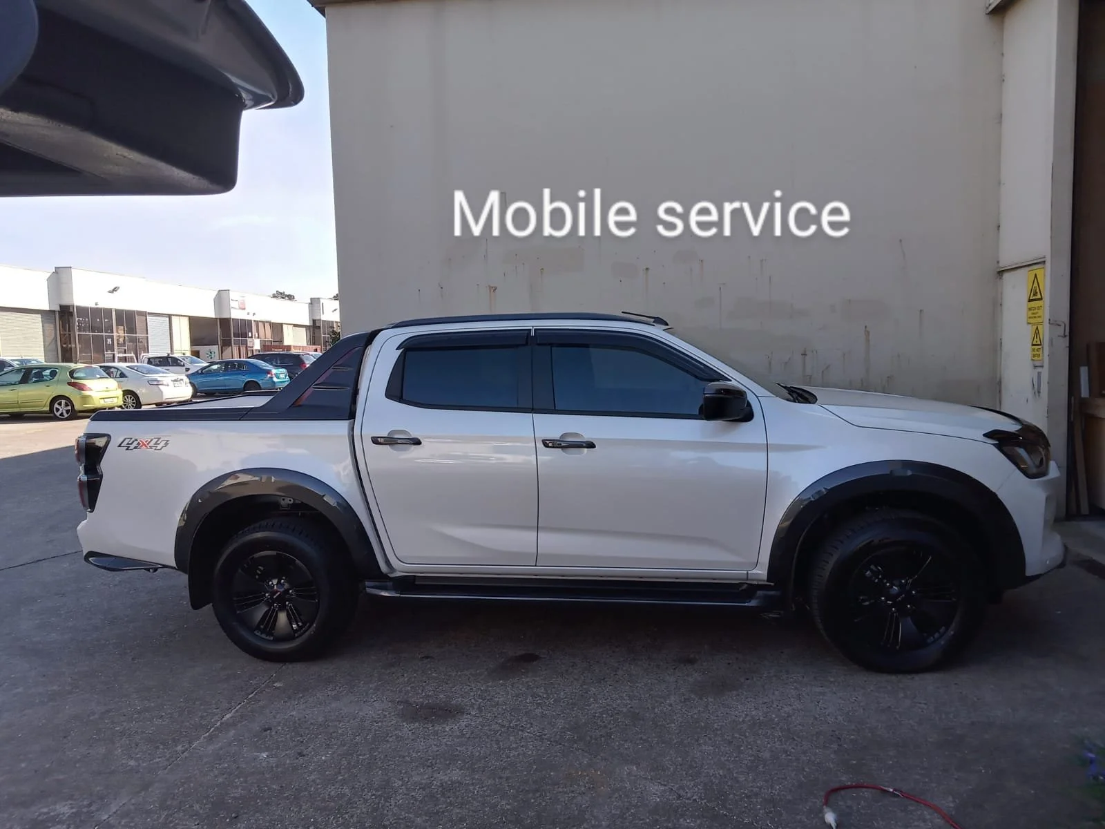 White pickup truck parked outside a building with a sign that reads 'Mobile service' on the wall.