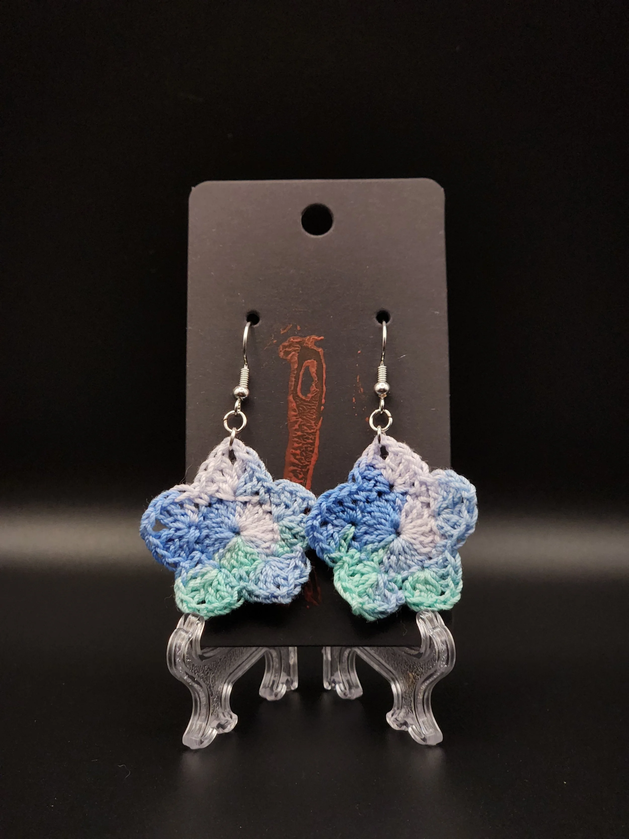 Colorful crocheted butterfly earrings with blue, green, and purple hues hanging on a black display card.