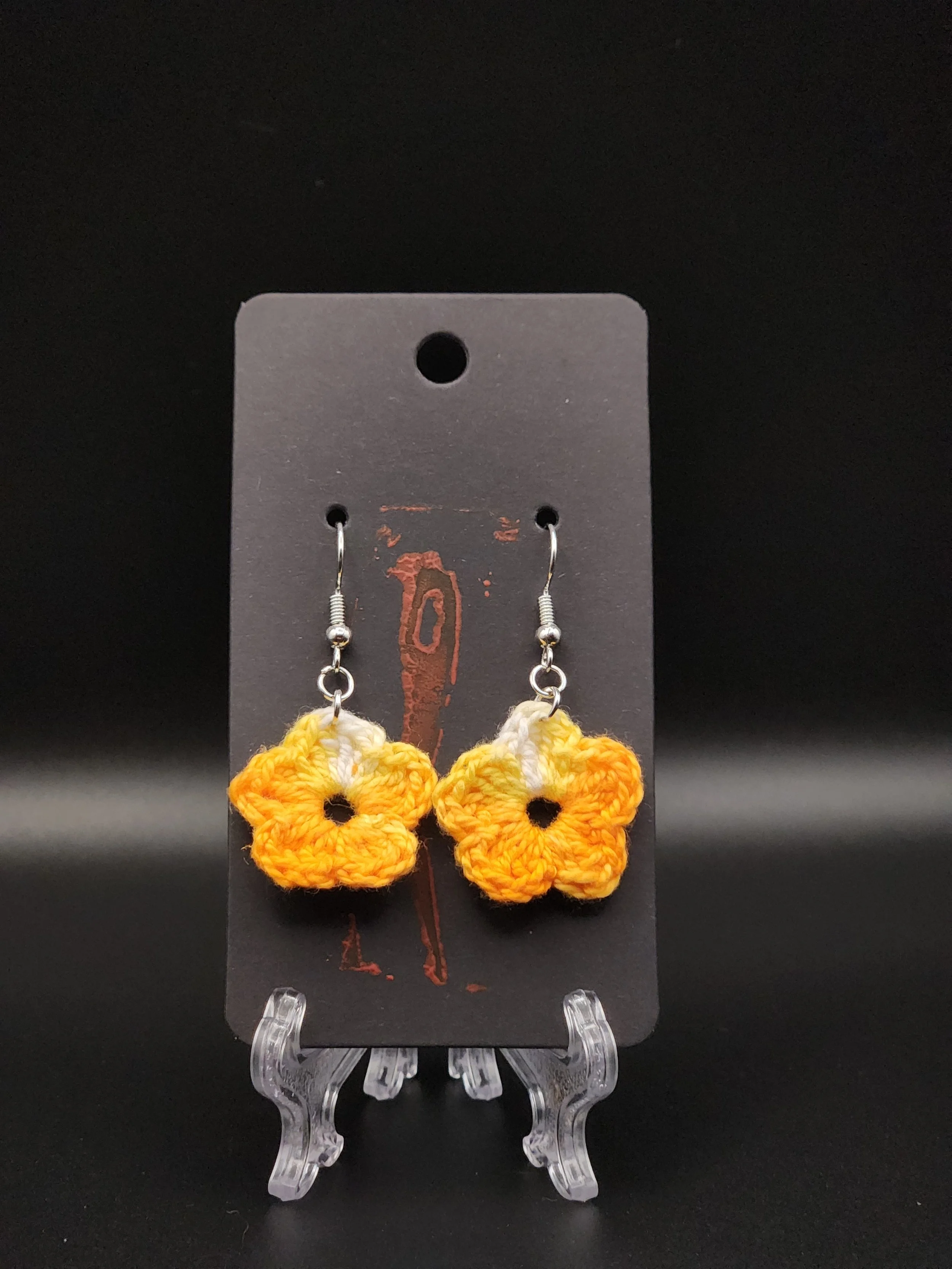 Yellow and orange crocheted flower earrings on a black display card.