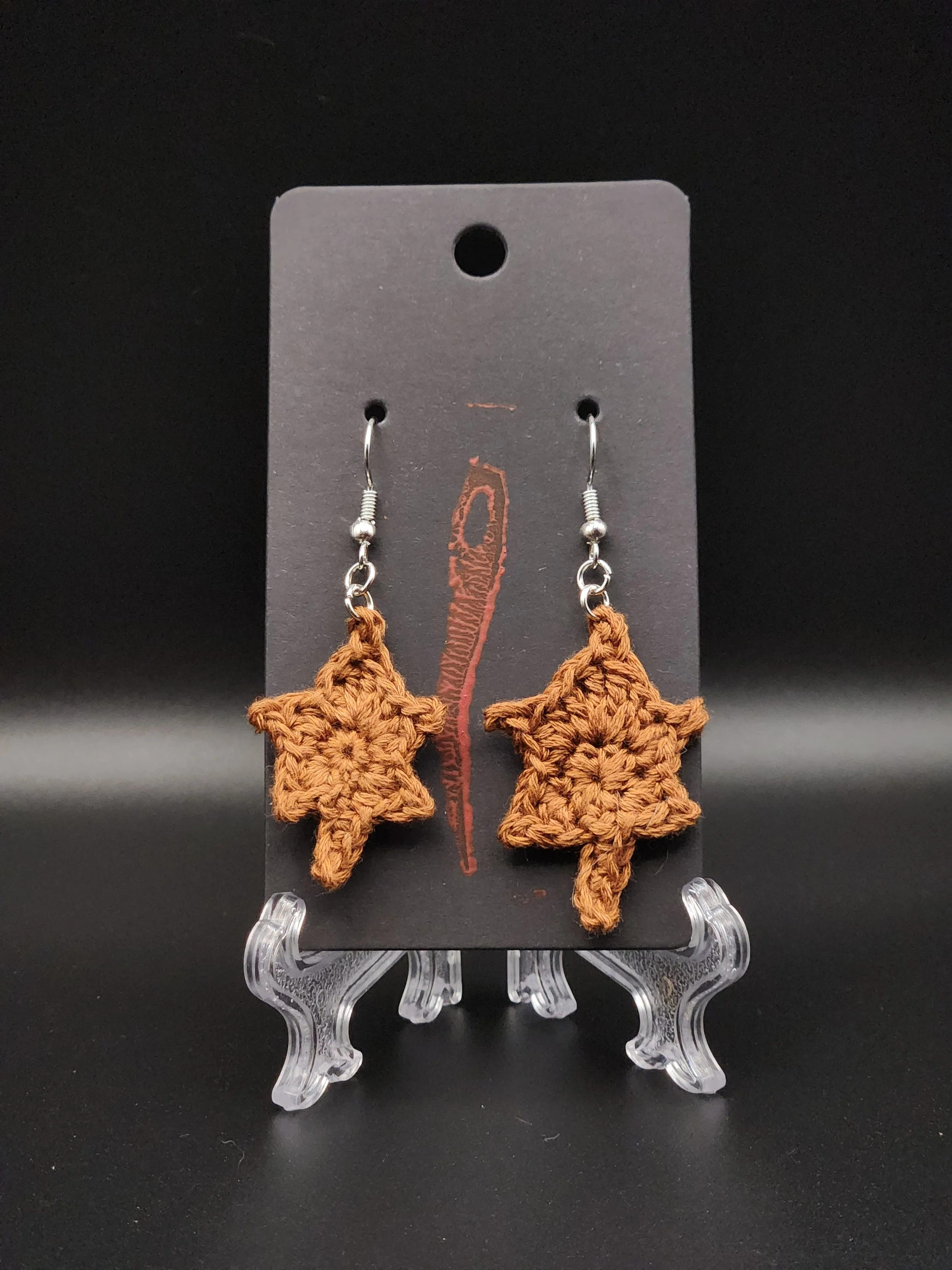 Crocheted brown star-shaped earrings on a black display card.
