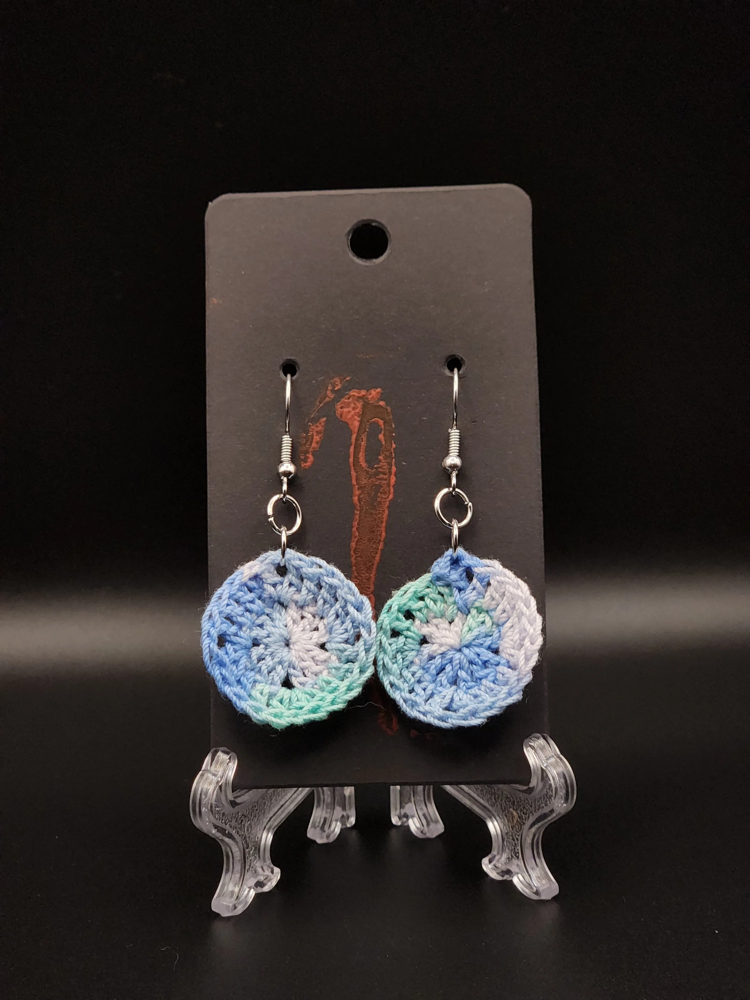 Colorful crocheted circle earrings on a black display card.