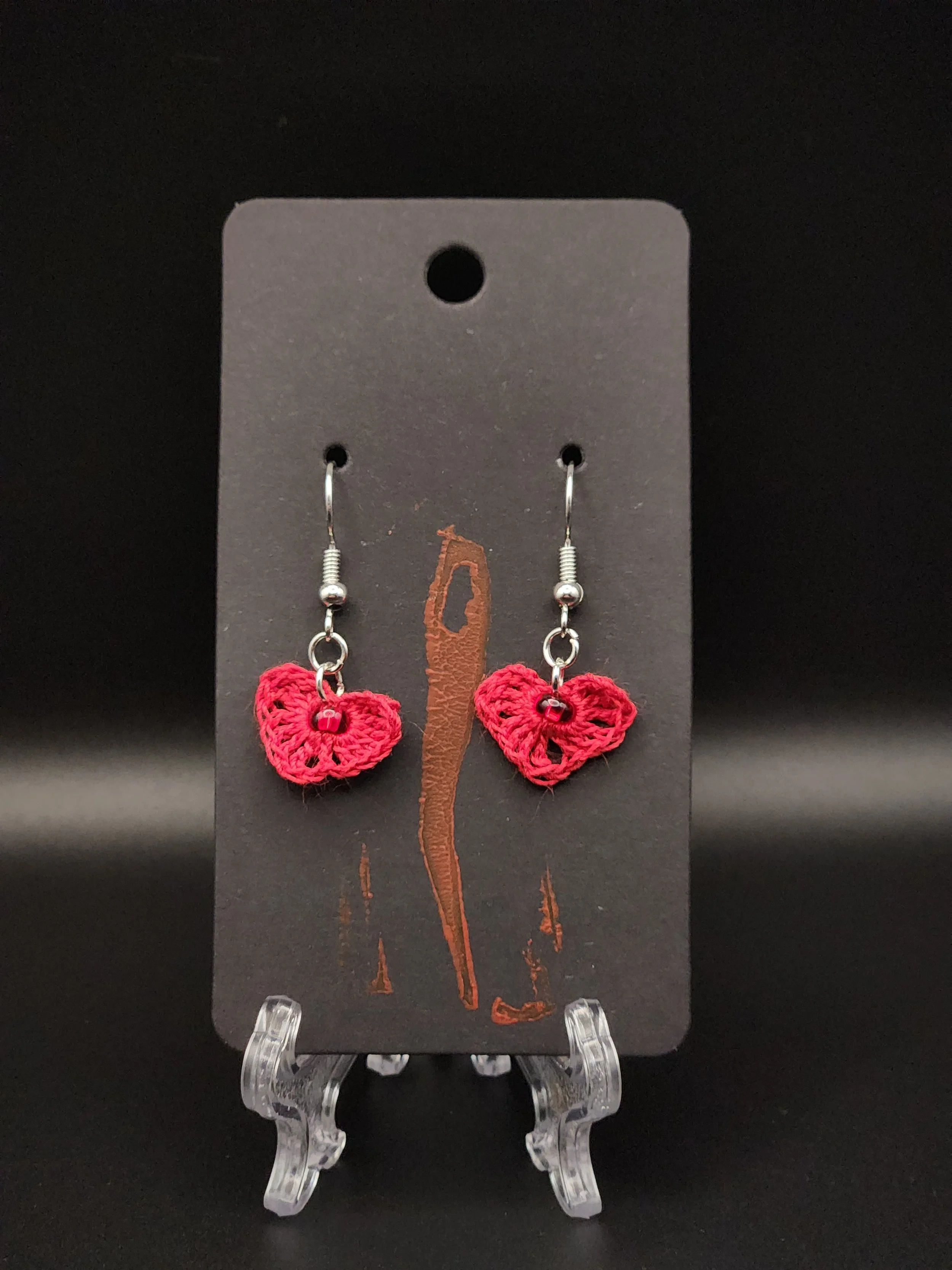 Pink crochet heart earrings with small red beads on black display card.