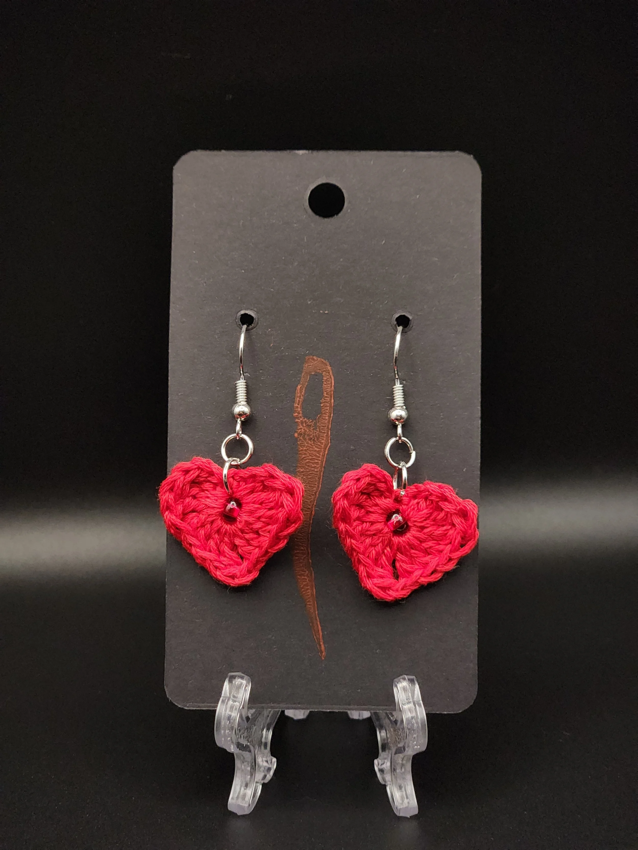 Red crocheted heart earrings on black display card.