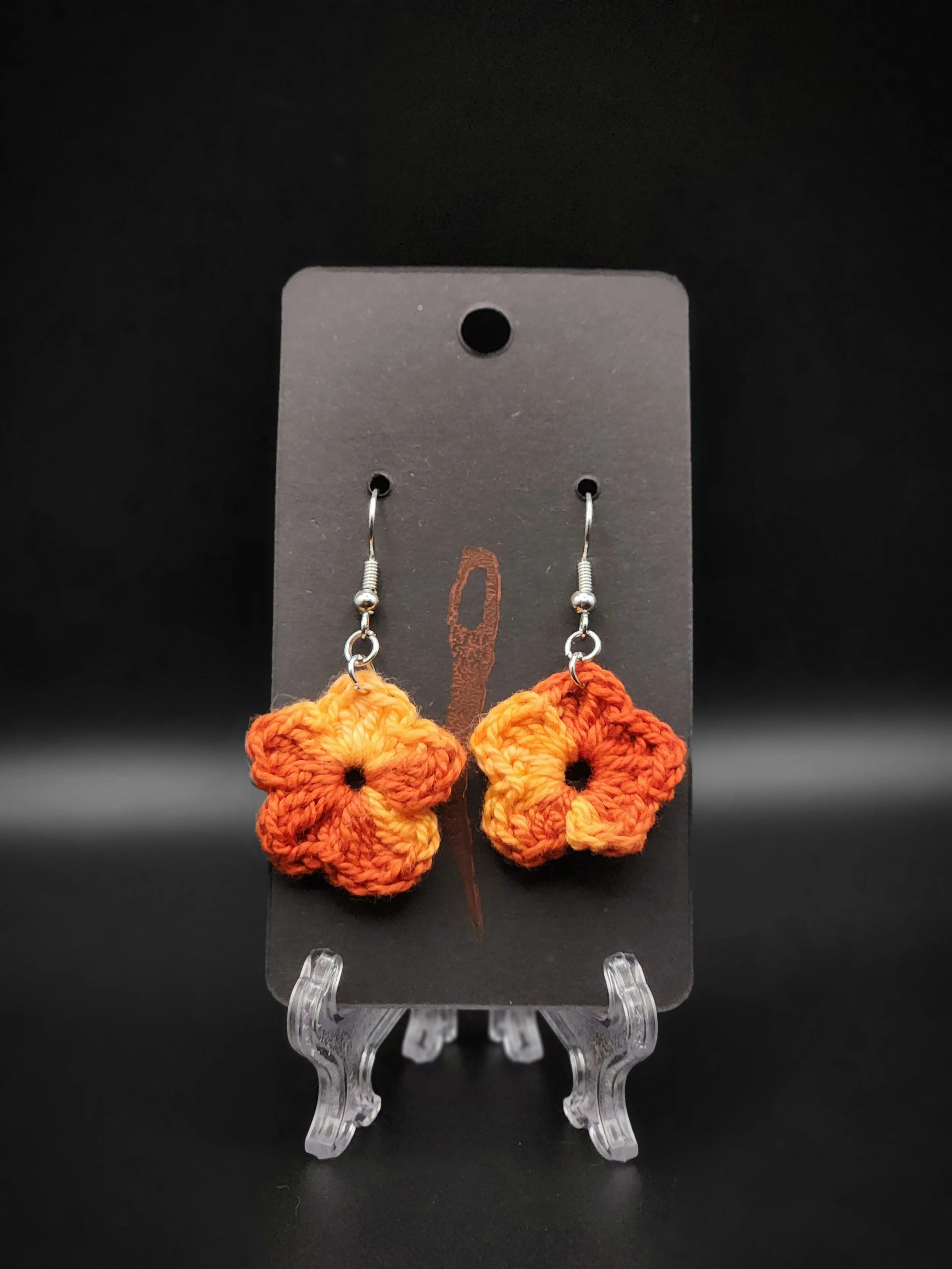 Pair of handmade crocheted orange and yellow flower earrings displayed on a black card.