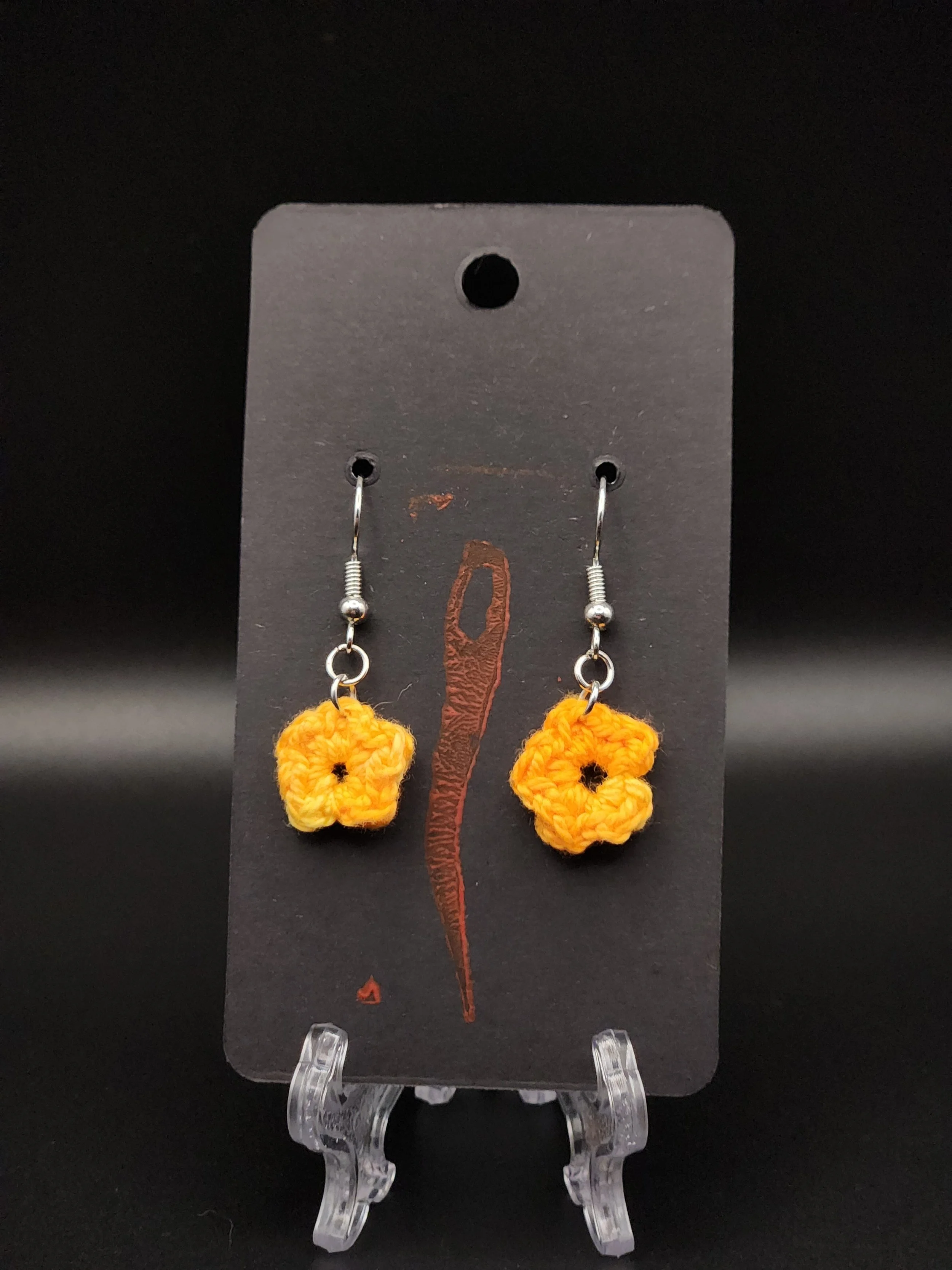 Yellow crochet flower earrings on black display card with a red and brown feather design.