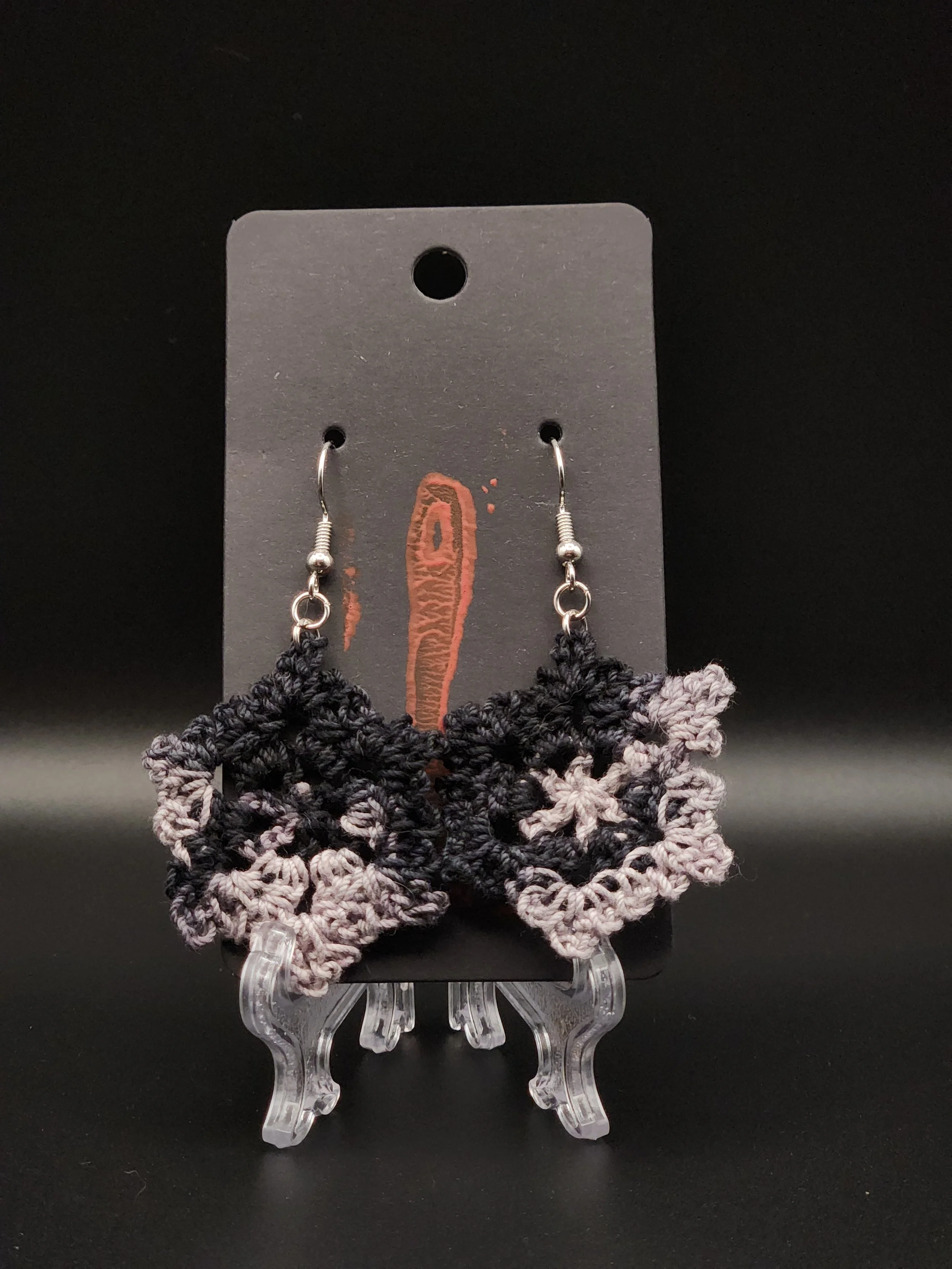 Black and gray crochet star-shaped earrings with metal hooks on a black display card.