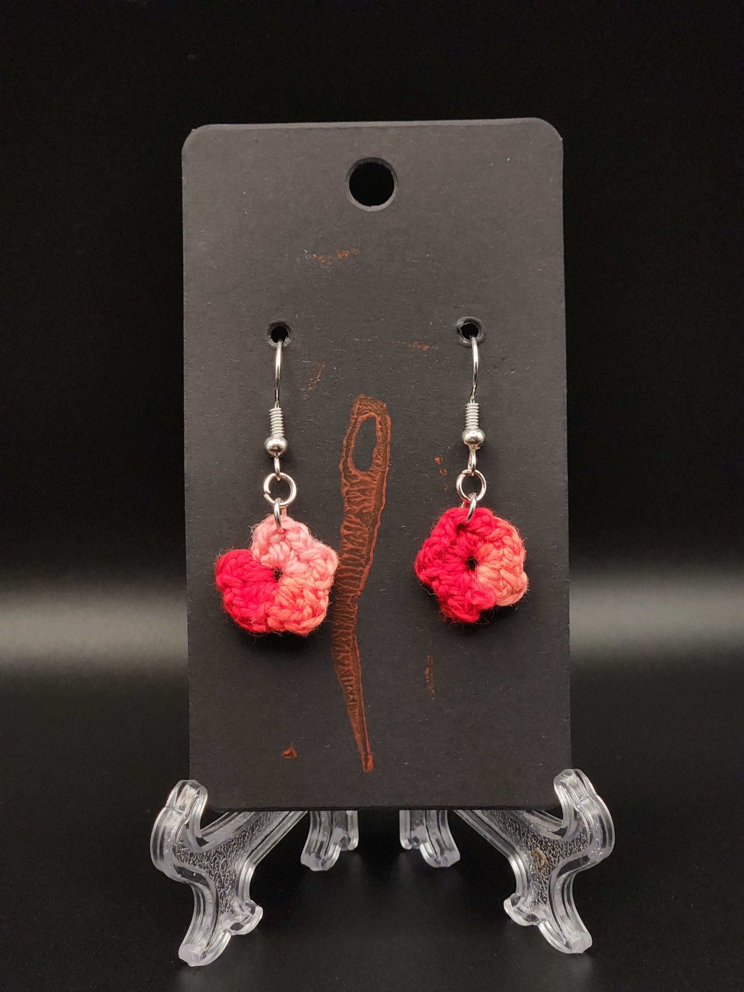 Red and pink crocheted flower earrings hanging on a black display card.