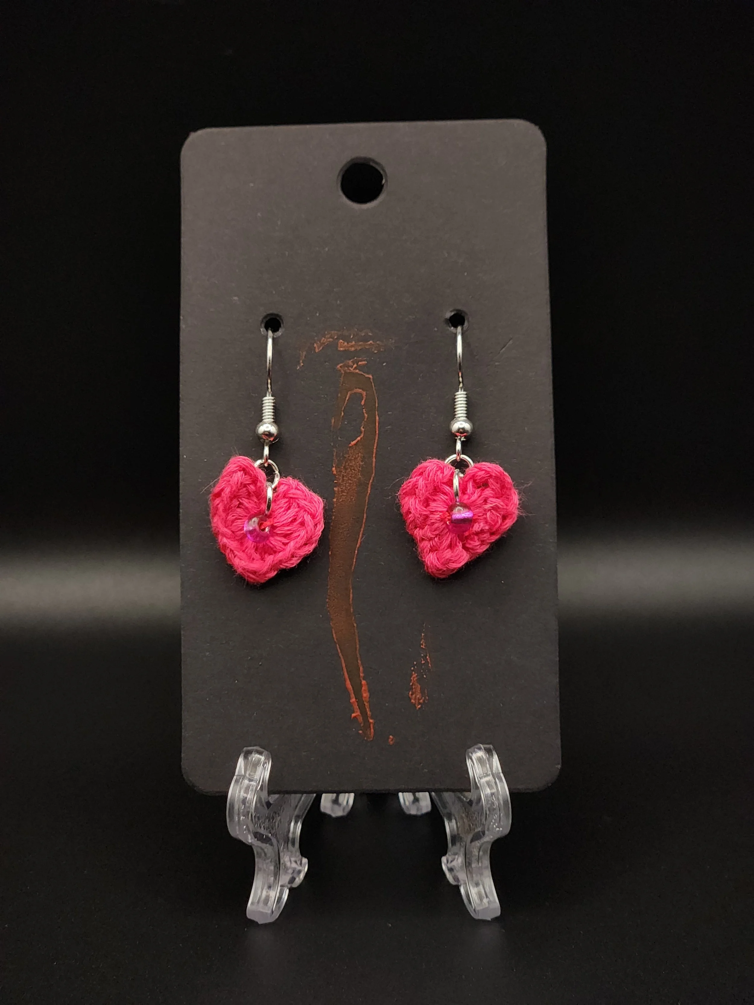 Pink yarn heart earrings displayed on a black jewelry stand