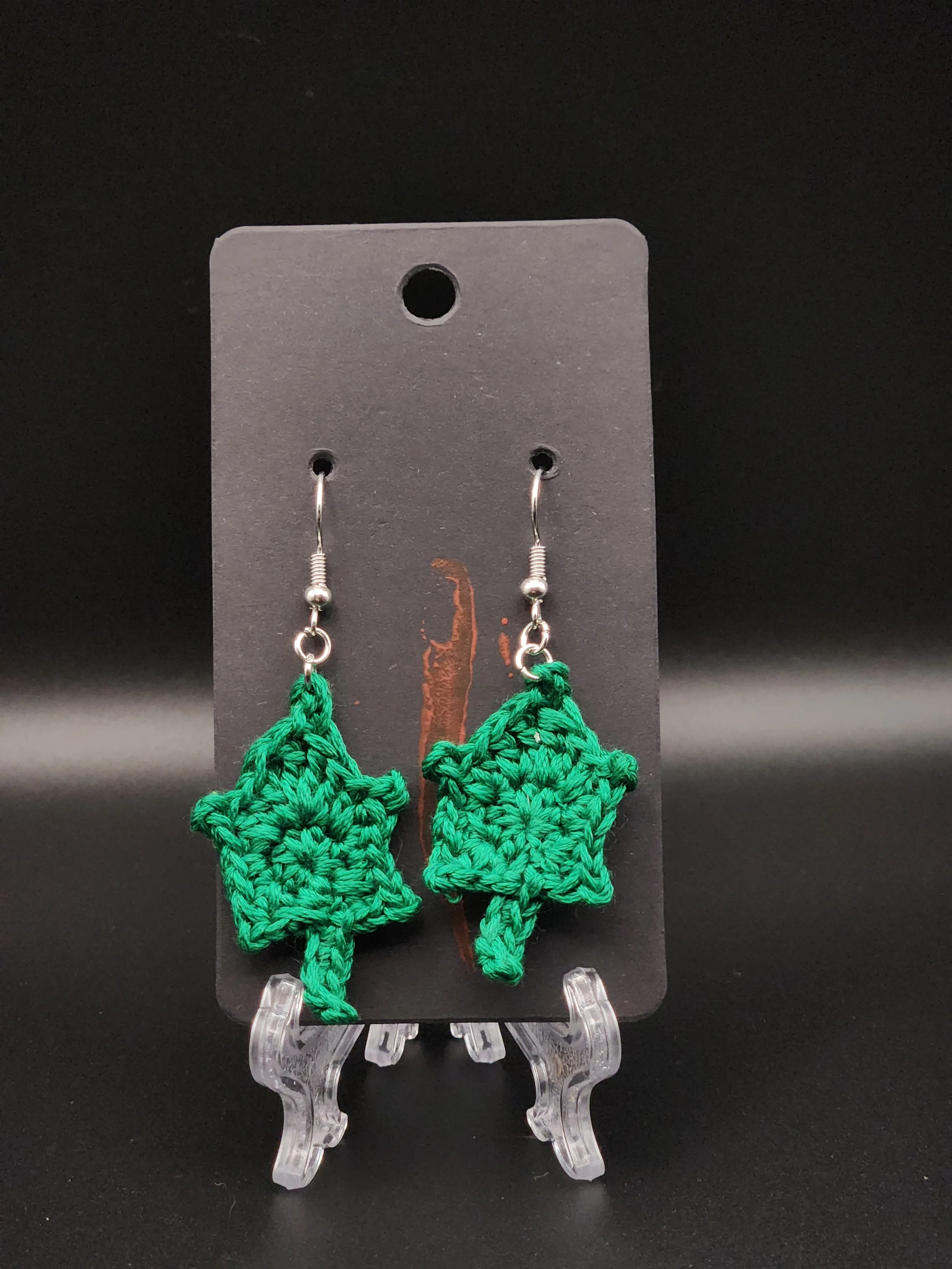 Green crocheted Christmas tree earrings on a black display card.