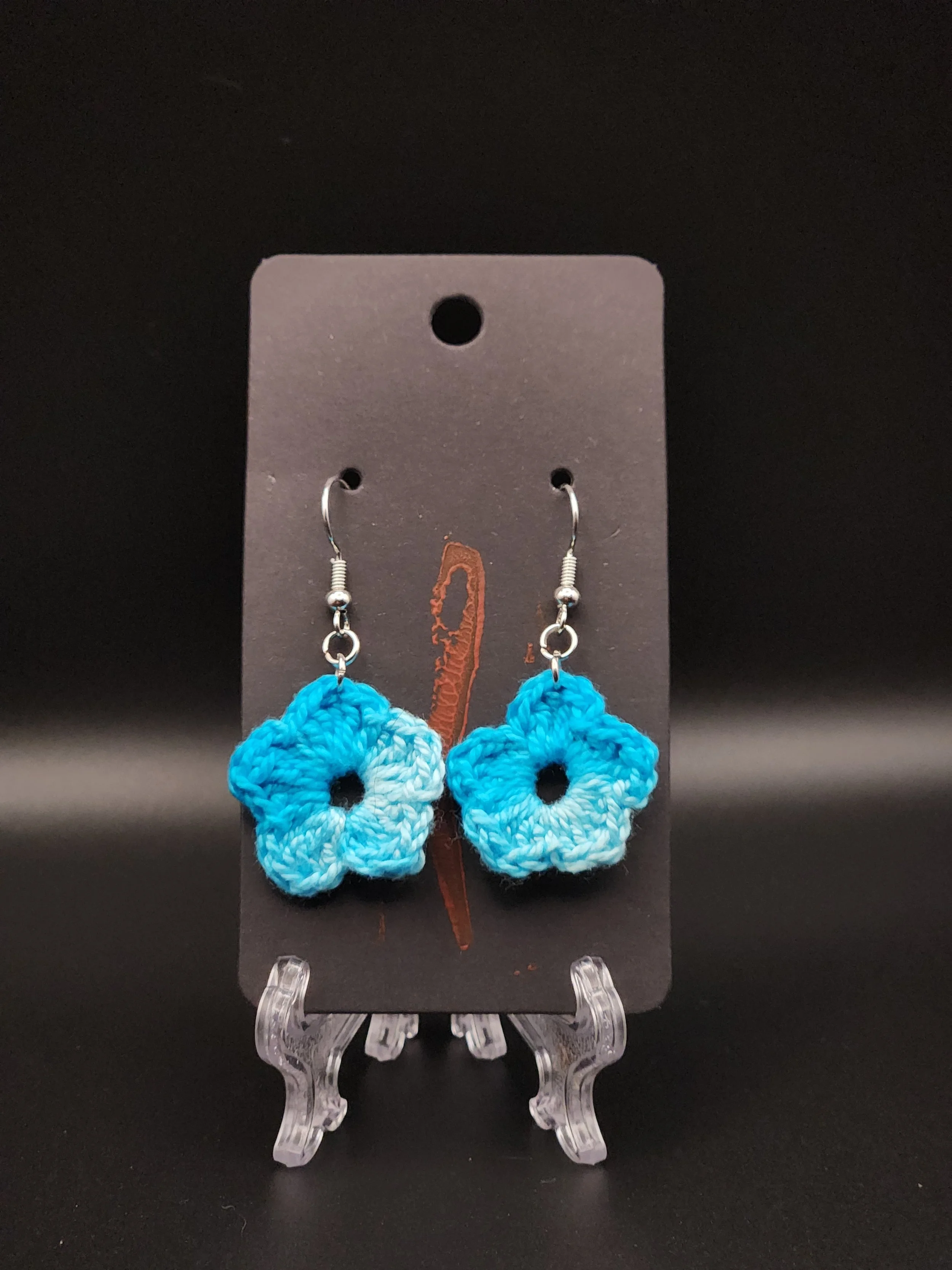 Blue crocheted flower earrings on black display card.