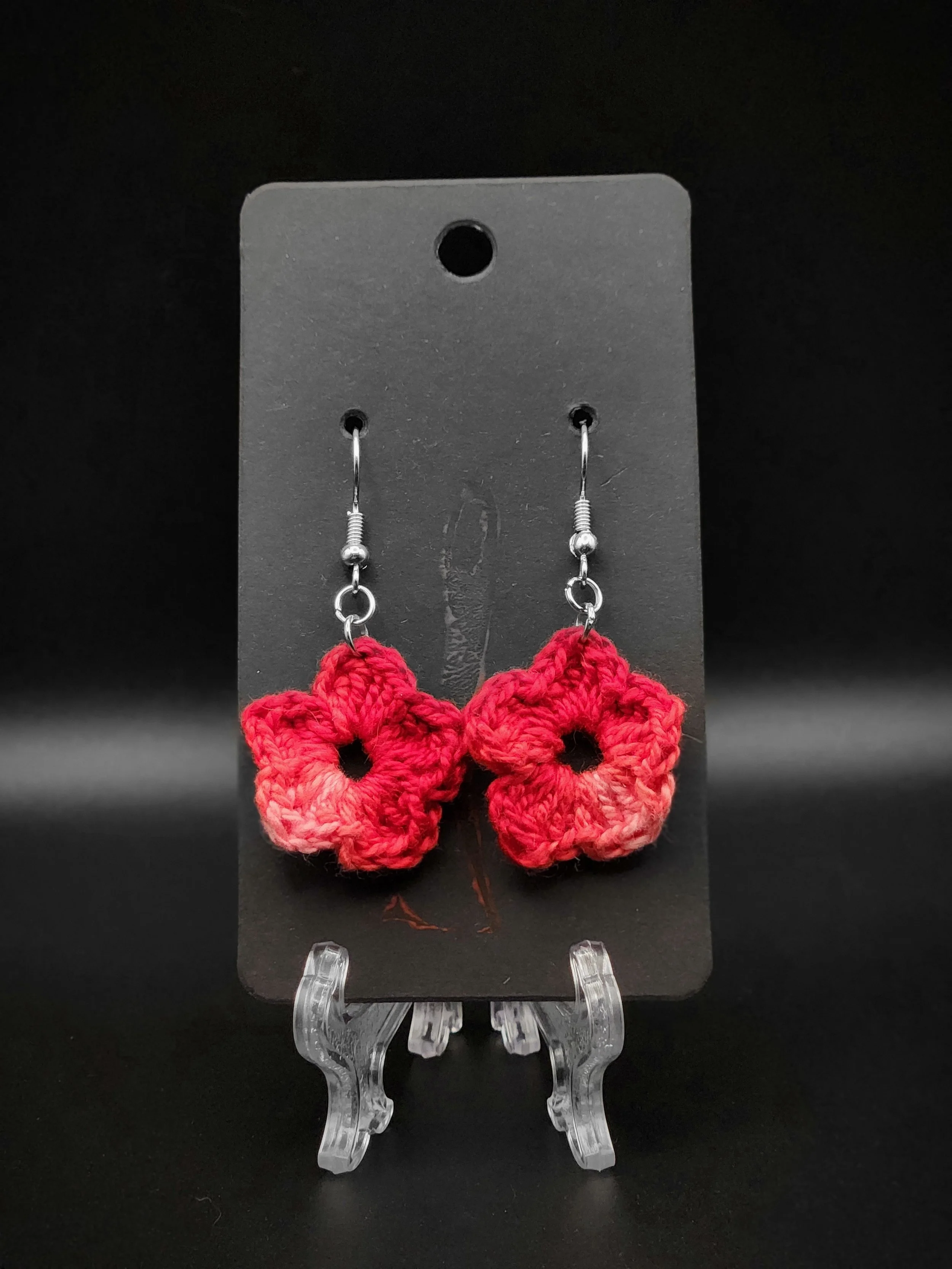 Red crocheted flower earrings on display with a black background.