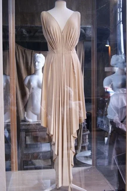 Robe rose poudré de Madame Grès exposée sur buste, drapée en V profond avec plis fluides et ourlet asymétrique.