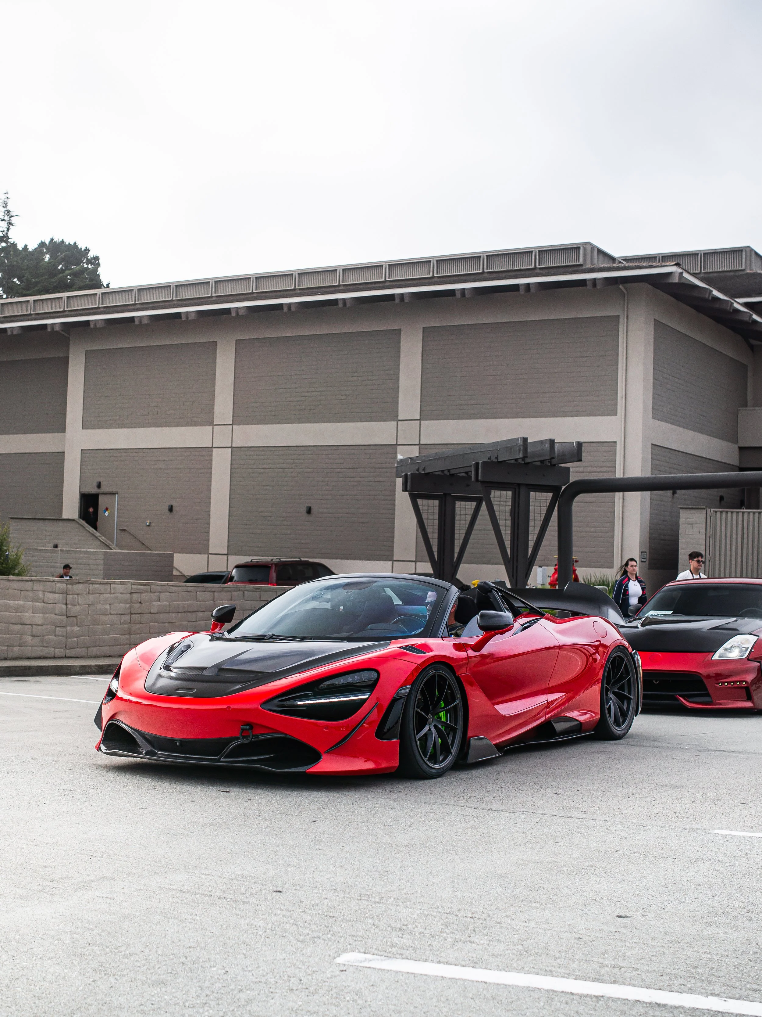 Red and black sports car parked in a lot with a modern building in the background.