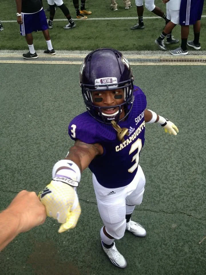 A young football player in uniform reaching out hands to shake while on the field.
