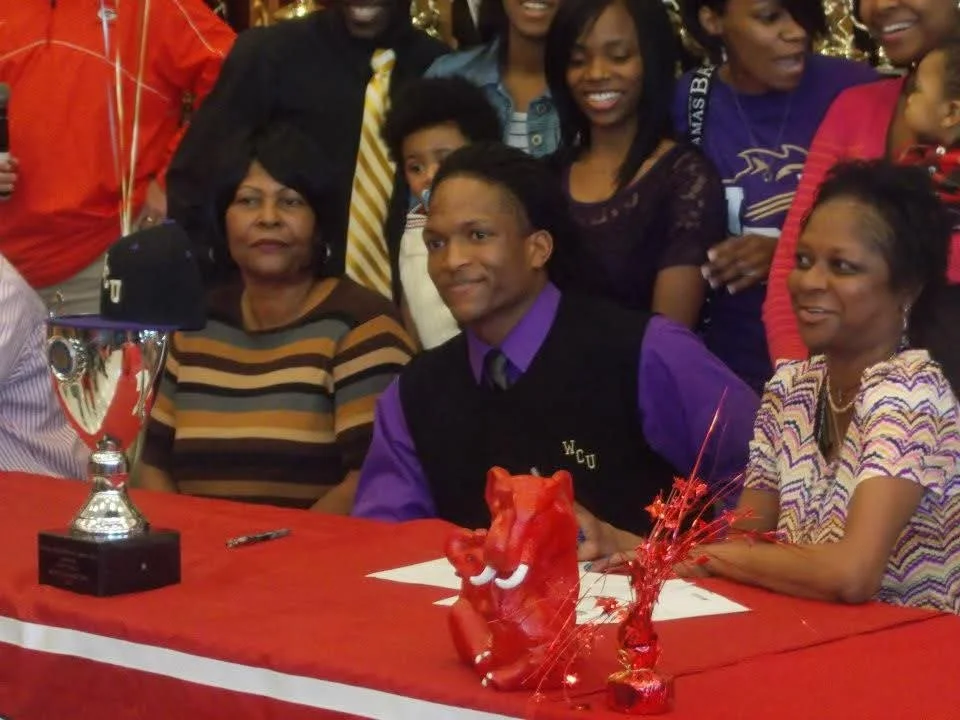 Group of people at a celebration taking a photo, with a table adorned with a trophy, a red tiger figurine, and red decorations.