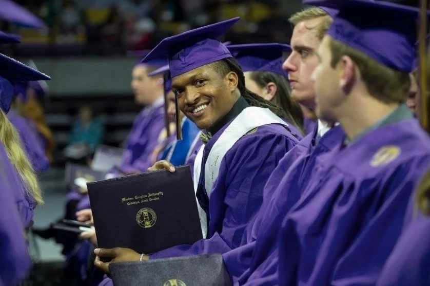 Graduate students wearing purple caps and gowns holding diplomas at a graduation ceremony.