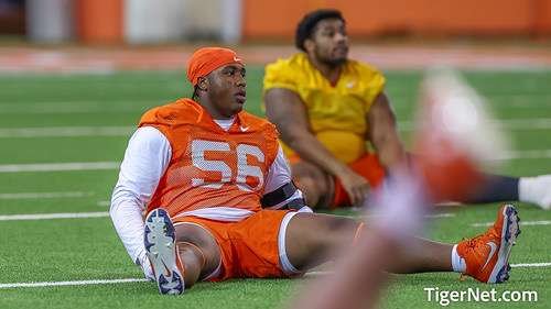 Two football players sitting on the field after a game, one in orange uniform with the number 56, and another in yellow uniform in the background.
