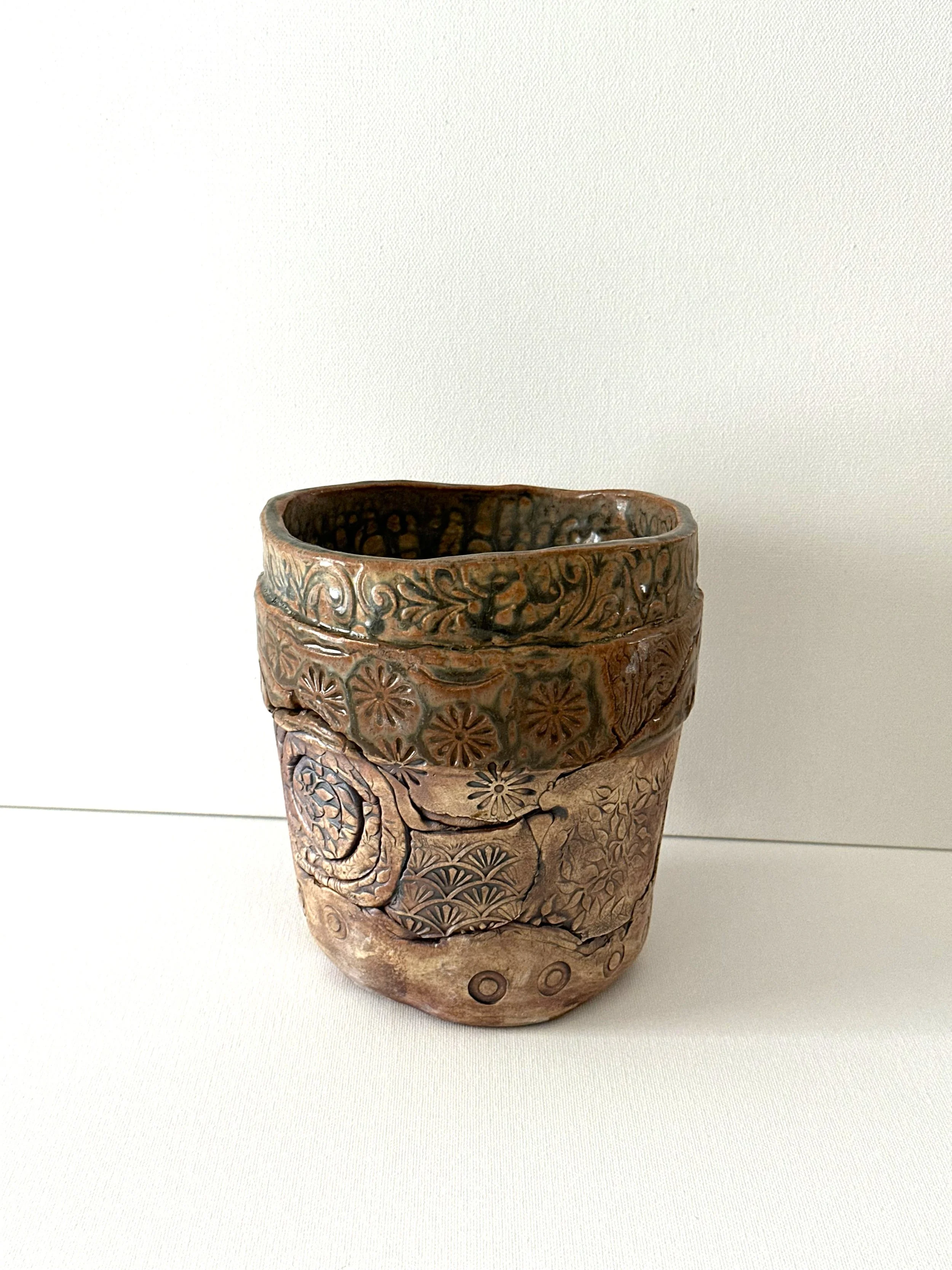 A layered porcelain clay flower pot finished with handmade stamped design elements. Brushed with Iron Oxide and finished with a Santorini Ash glaze.