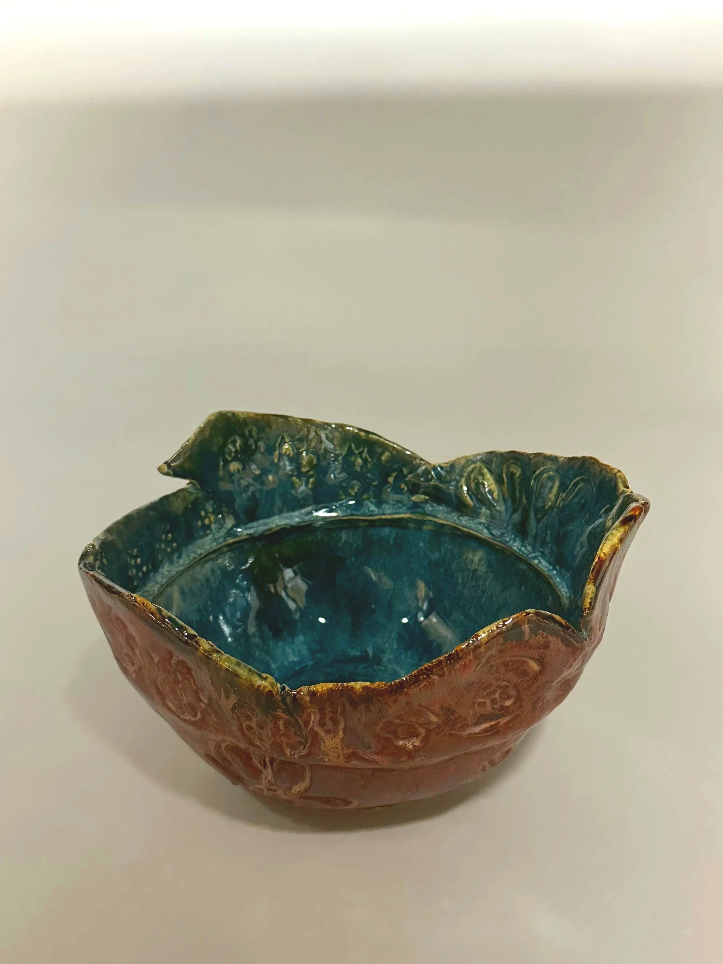 A large layered yarn bowl glazed with copper and eight layers of additional glazes, finished with handmade stamps for added texture and depth. A yarn hole makes this piece functional for your crafts.