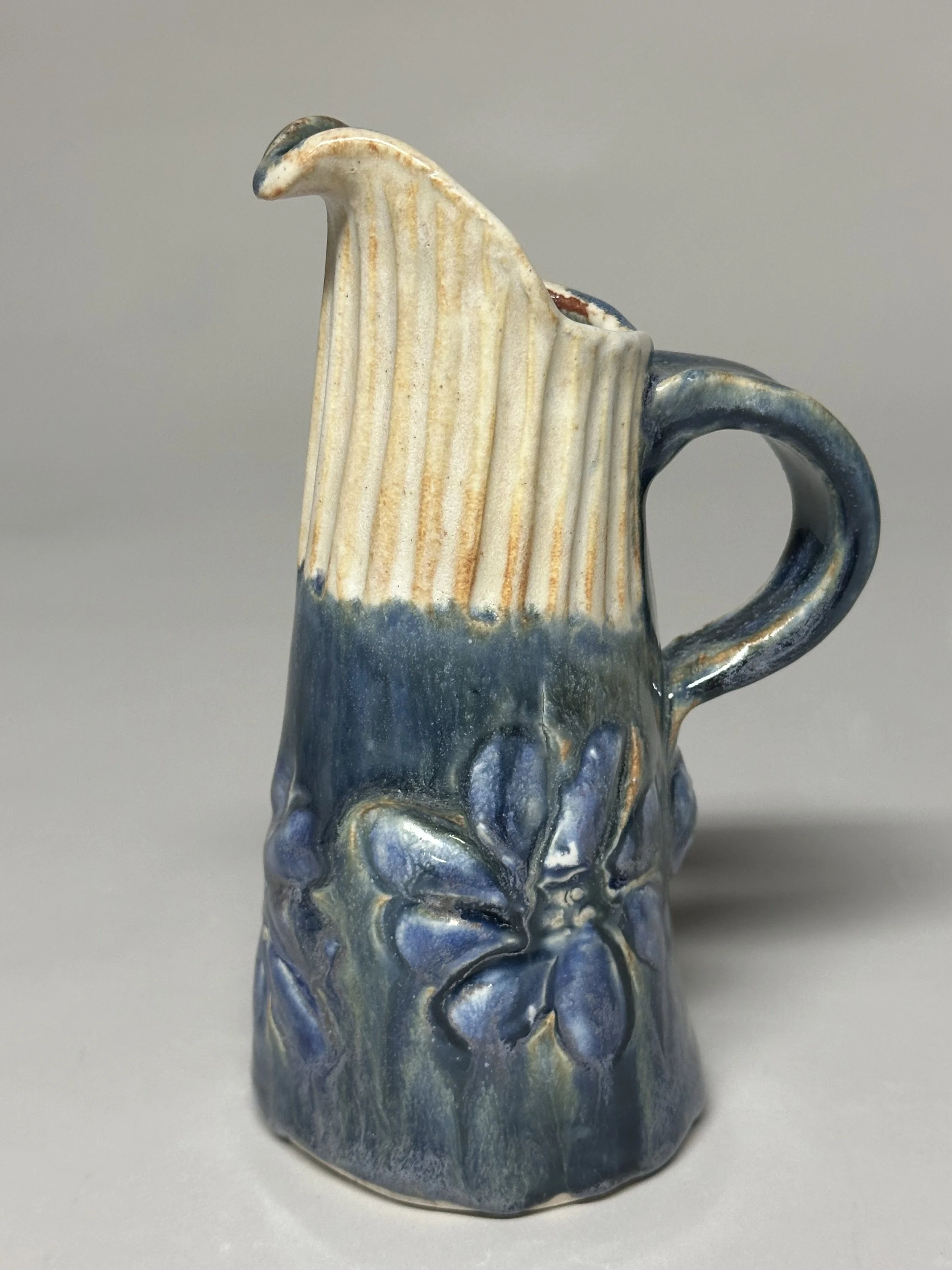 A small pitcher glazed with Ash Blue and Shino, finished with a hand‑carved top and handmade stamps for added texture and charm.