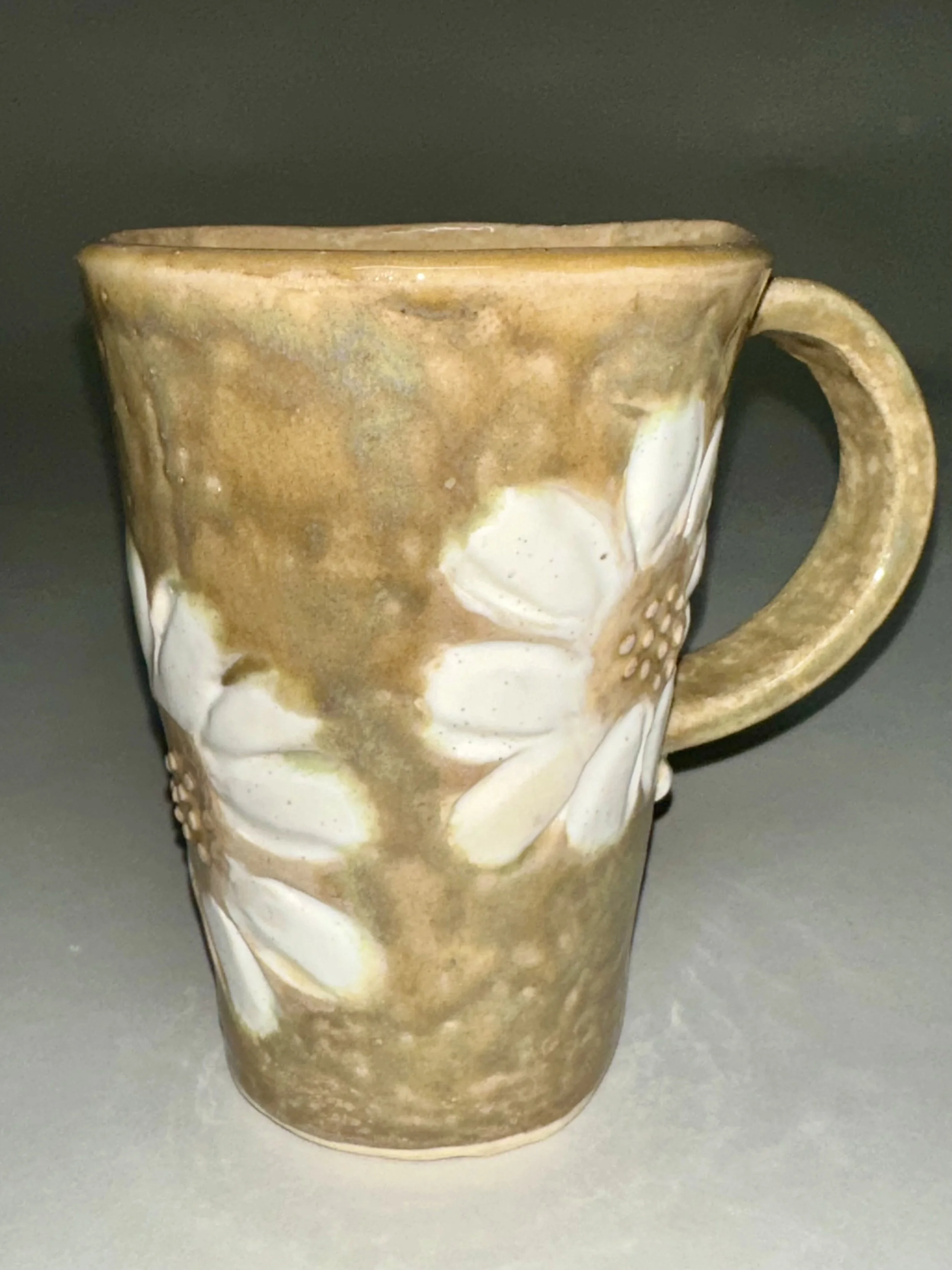 Handbuilt from porcelain clay, this mug features carved stamp impressions inspired by Michigan’s wild daisies. The earthy glaze and raised floral details create a tactile piece of art for coffee and tea.