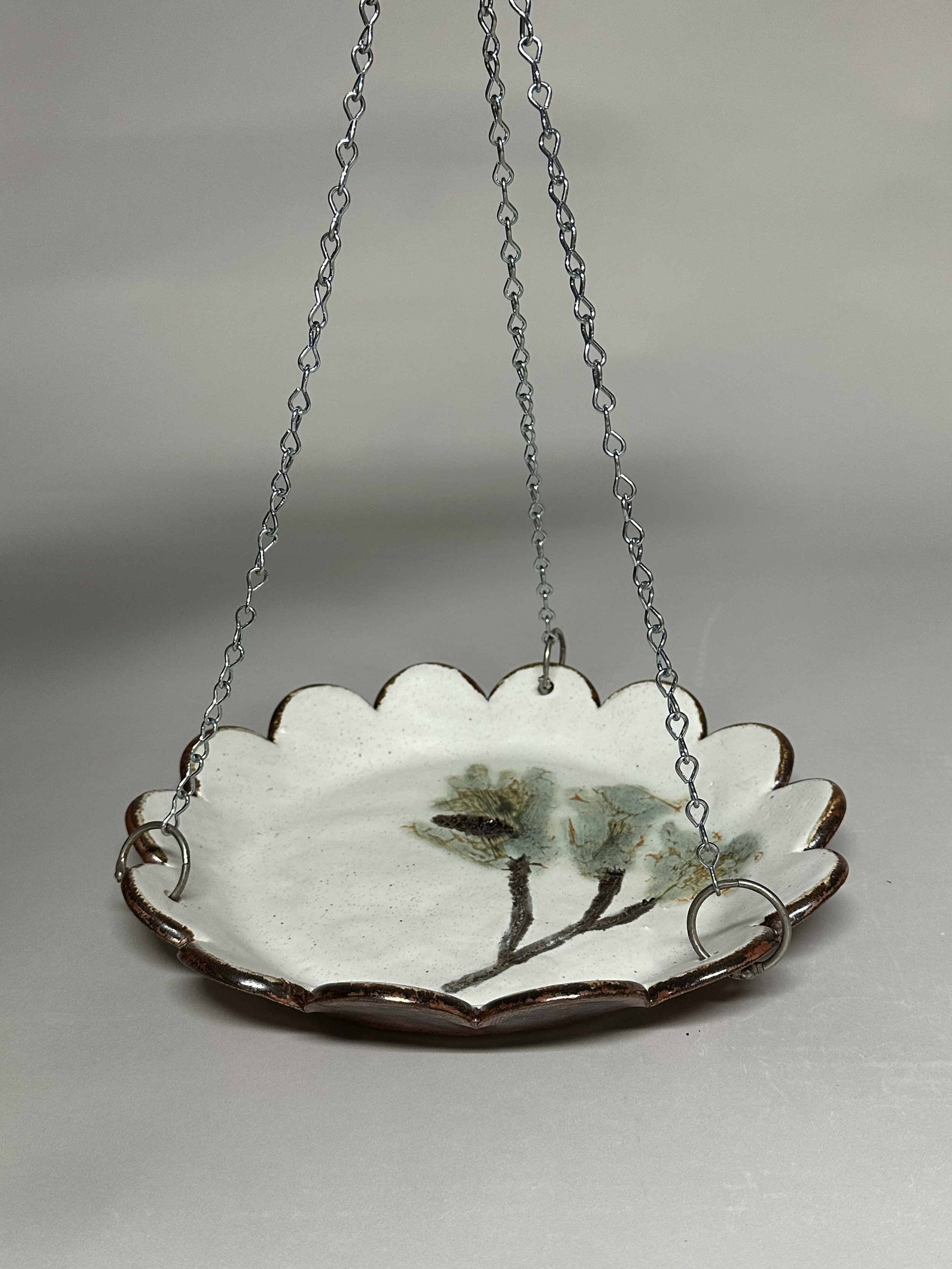 This bird feeder is hand crafted with pine impressions inspired by Northern Michigan, finished in a soft oatmeal glaze with a warm copper underside for a natural, woodland feel.