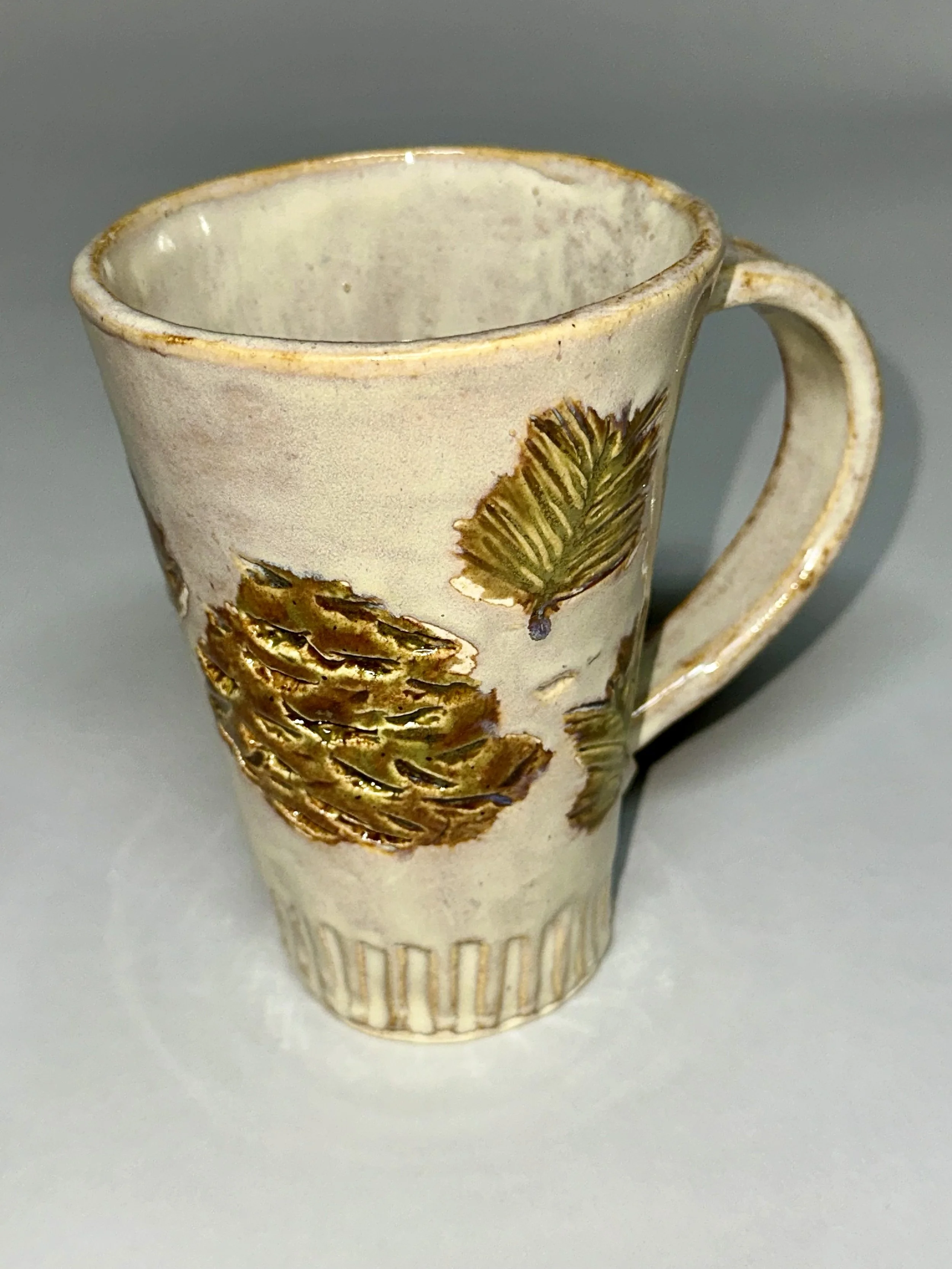 Crafted by hand, this ceramic mug showcases hand-carved stamp textures inspired by Michigan’s iconic pine trees. The natural glaze palette and sculptural details bring the forest to your fingertips, grounding every sip. 