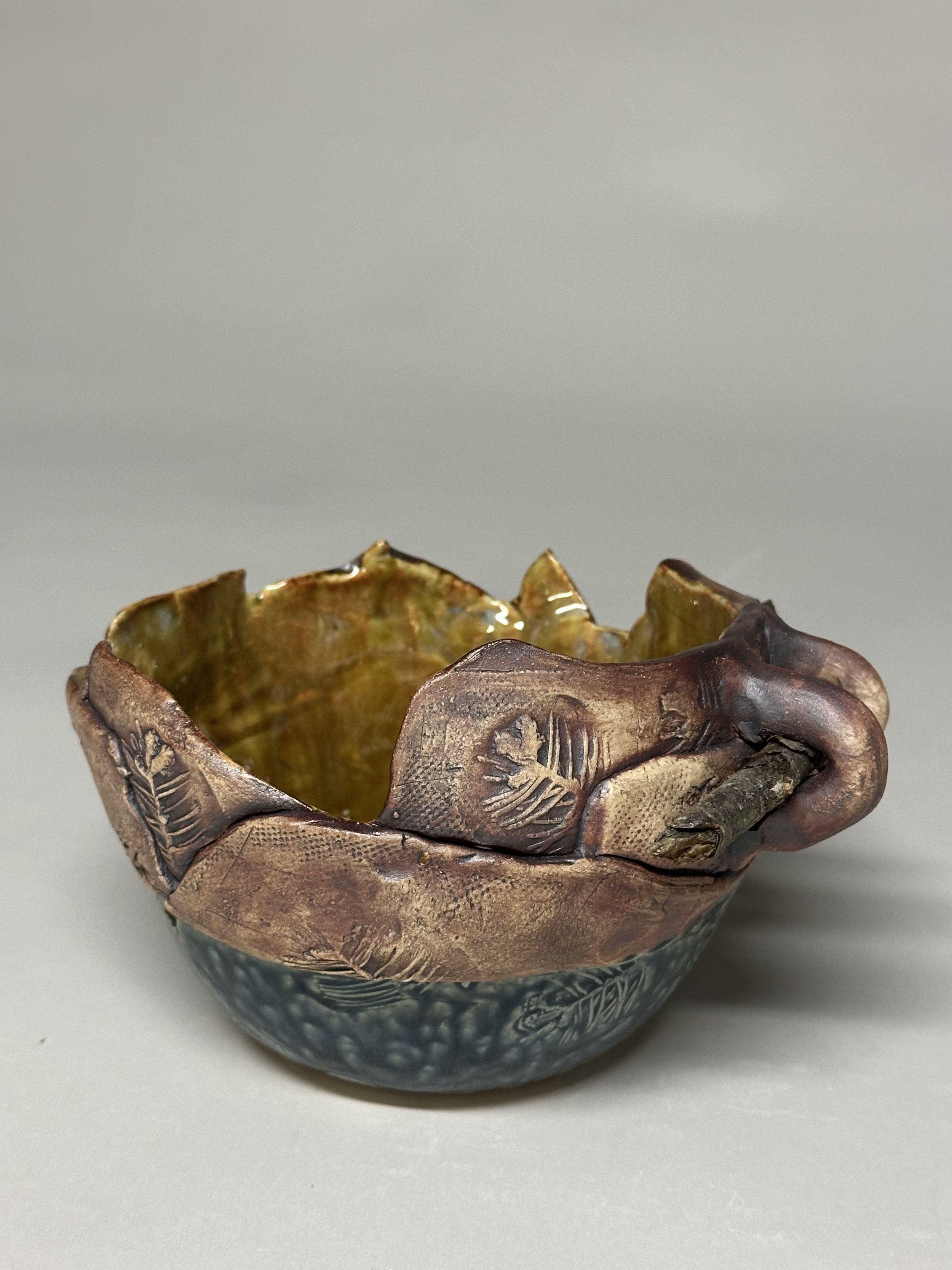 A handcrafted bowl glazed with iron oxide, Blue Ash, and eight layered glazes, finished with handmade stamps and a small birch branch to honor Michigan.
