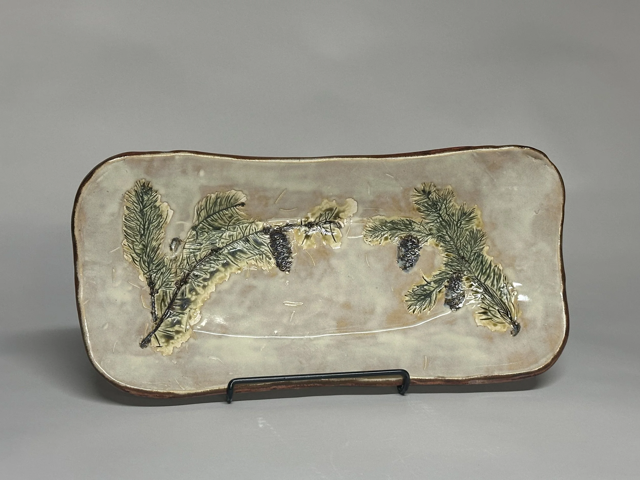 This baguette bowl is hand crafted with Northern Michigan pine branches and pine cones, featuring a soft birch glaze inside and a copper‑glazed underside for a warm, earthy finish.