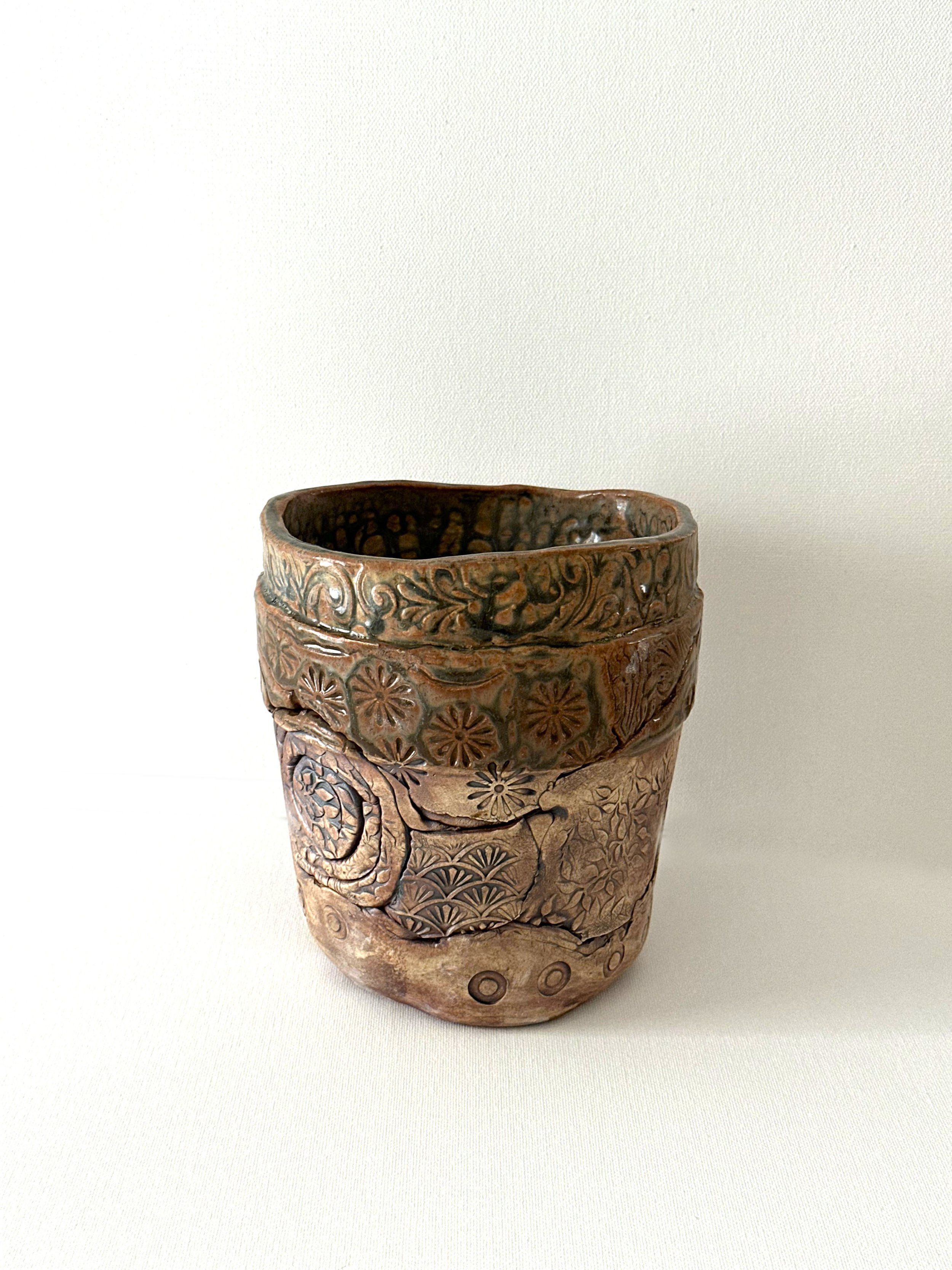 A layered porcelain clay flower pot finished with handmade stamped design elements. Brushed with Iron Oxide and finished with a Santorini Ash glaze.