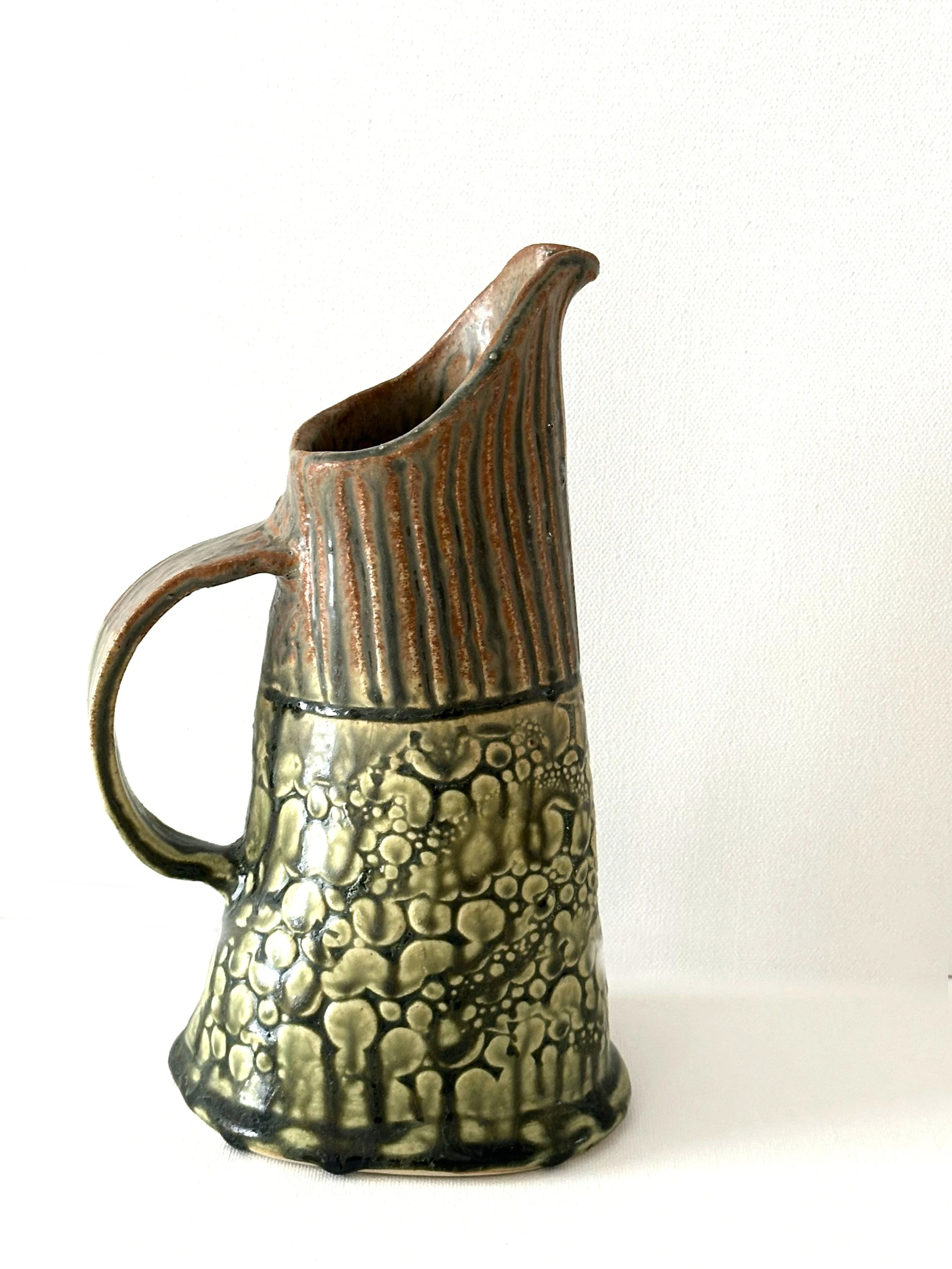 This lovely porcelain clay pitcher can be used to hold beverages. It is finished with a Santorini Ash glaze.