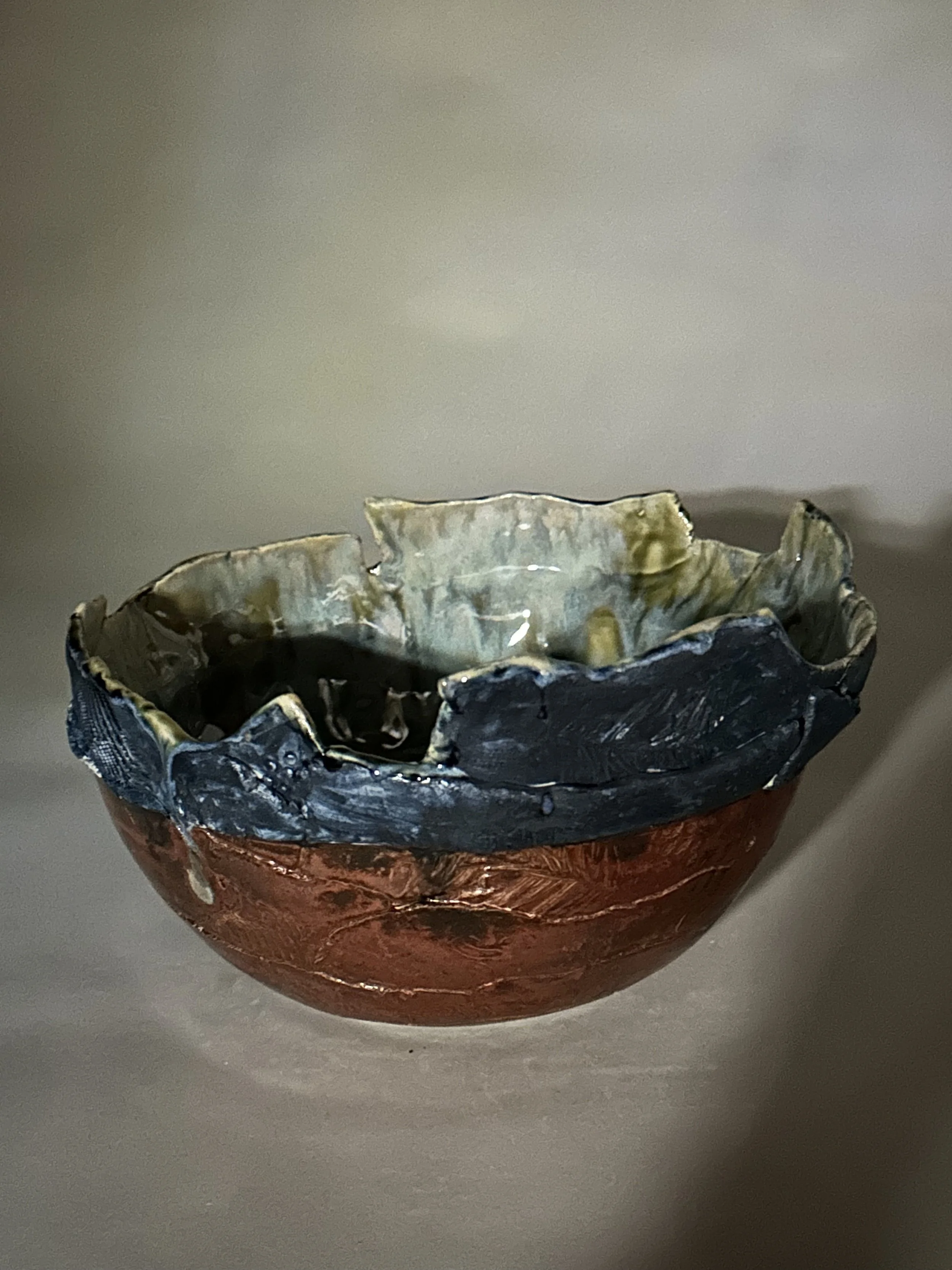 A large, layered hand‑built bowl that shimmers on the outside with rich copper and deep cobalt. Inside, eight layers of glaze flow over handmade stamps, creating depth, movement, and a woodland warmth that feels rooted in Michigan.