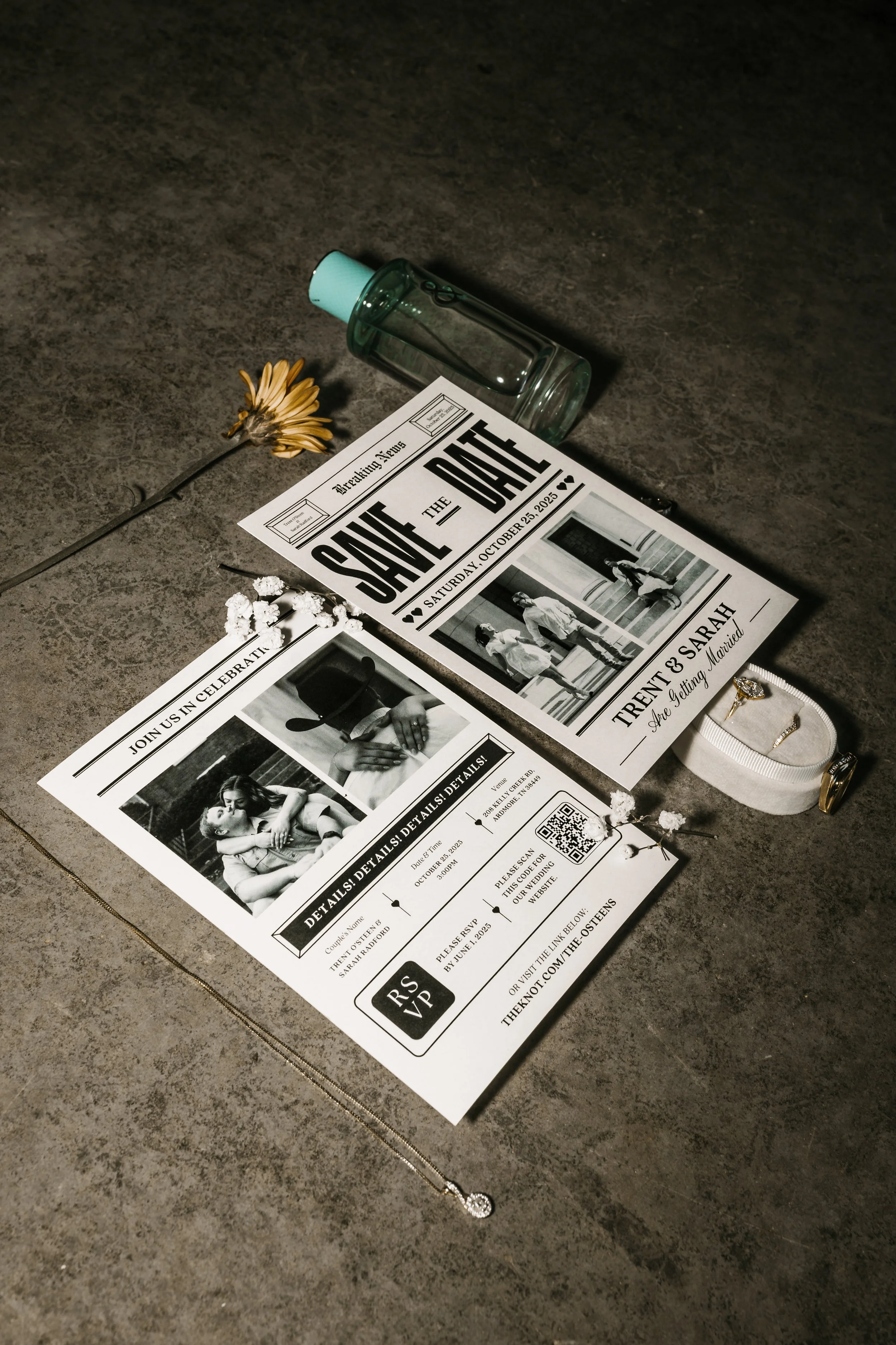 A wedding invitation, a glass bottle, a jewelry box with rings, a flower, some white embellishments, a small beige pouch, and a bottle of hand sanitizer are arranged on a dark textured surface.