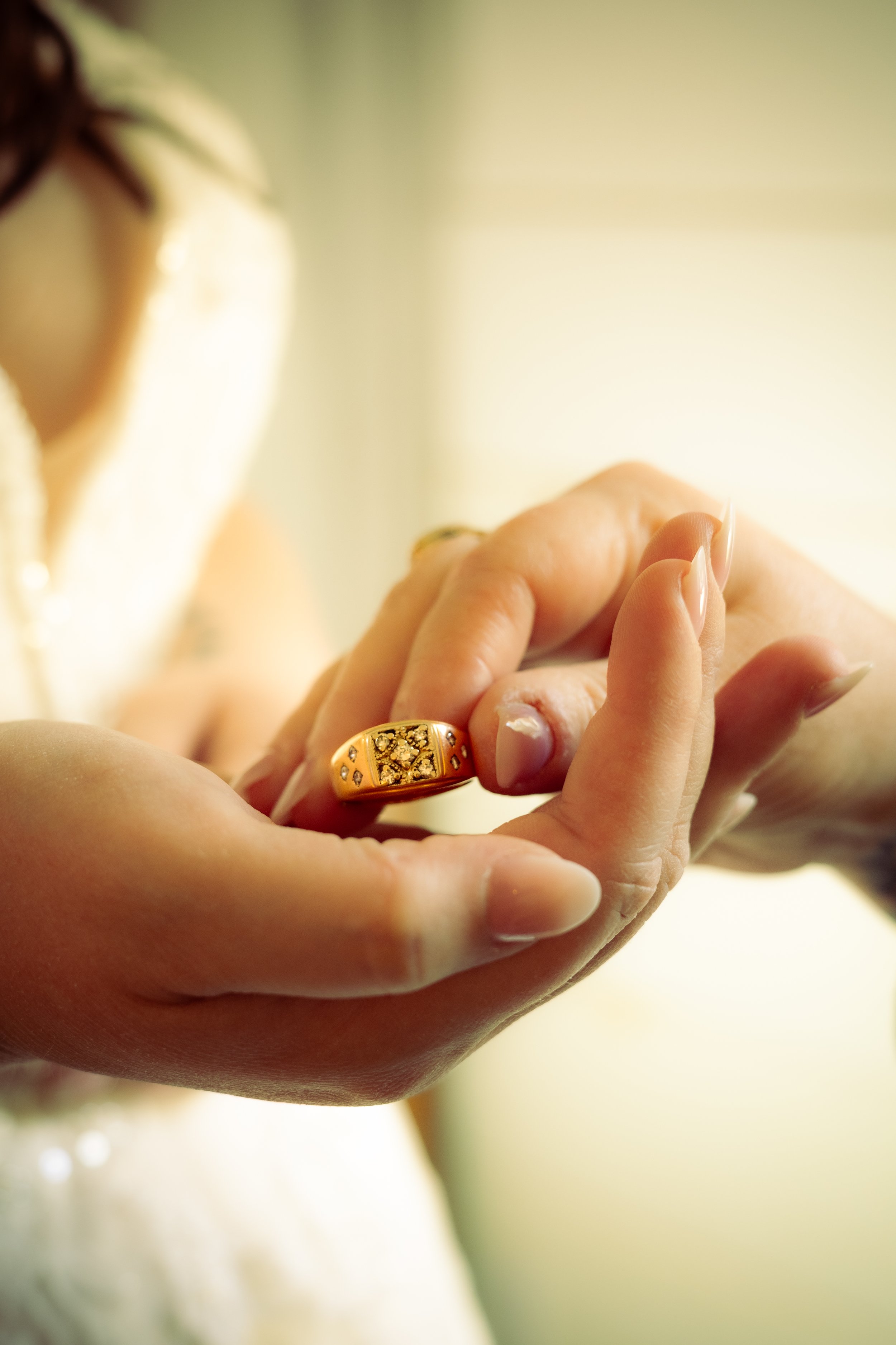 Close-up of a person wearing a gold ring, holding her hands together with fingers intertwined, soft natural lighting.