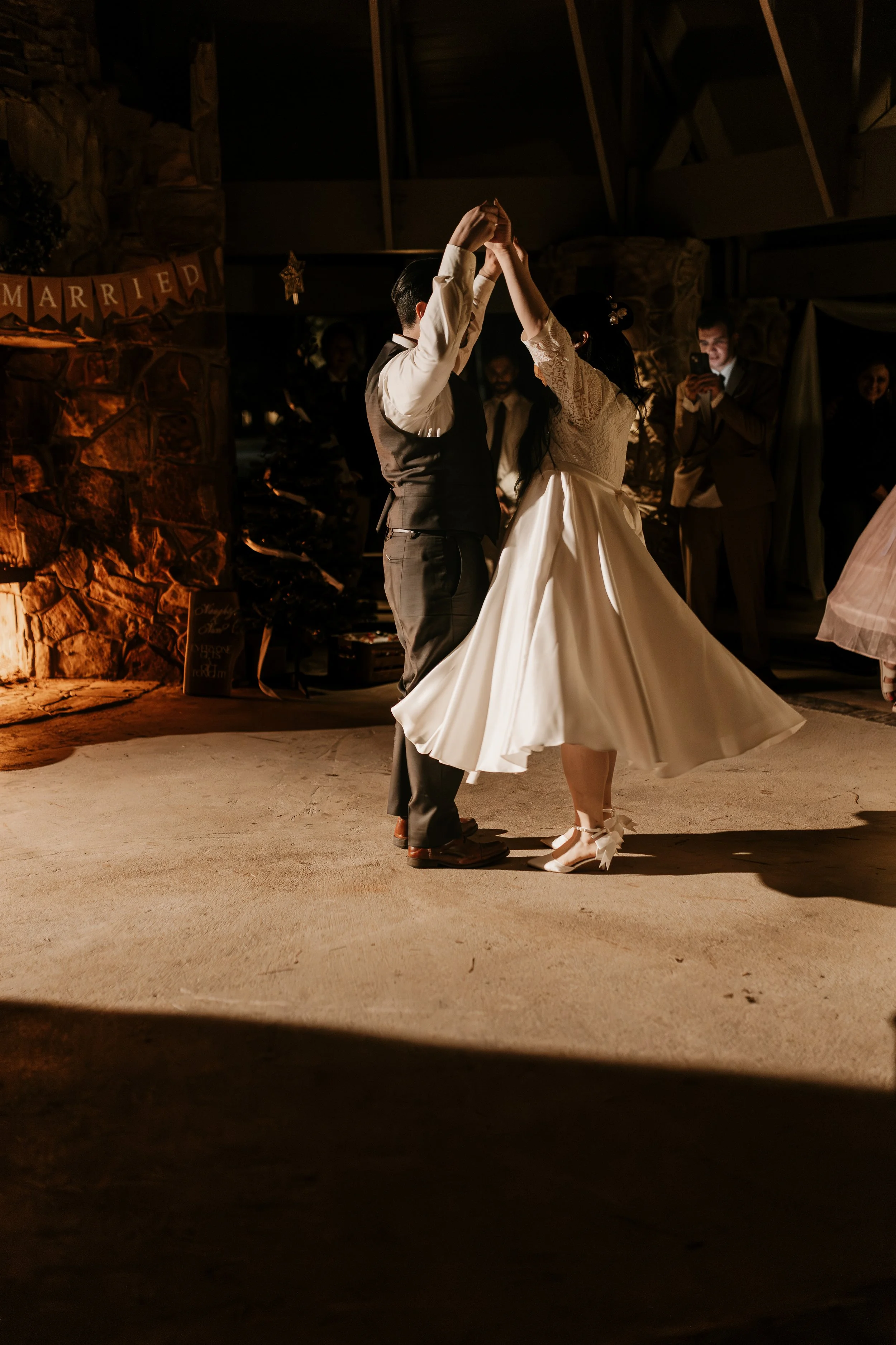 A bride and groom dancing at a wedding reception with guests watching, while some guests are taking photos.