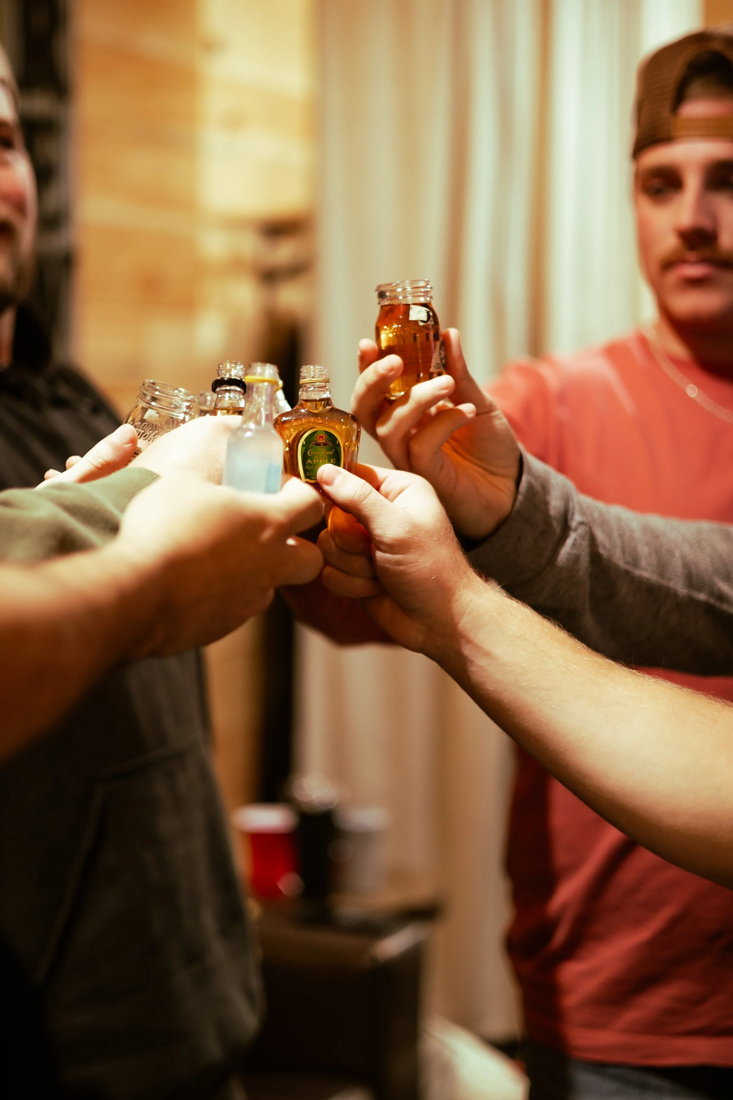 Group of people making a toast with bottles of alcoholic drinks in a cozy indoor setting. Unique wedding Photography in Mississippi.