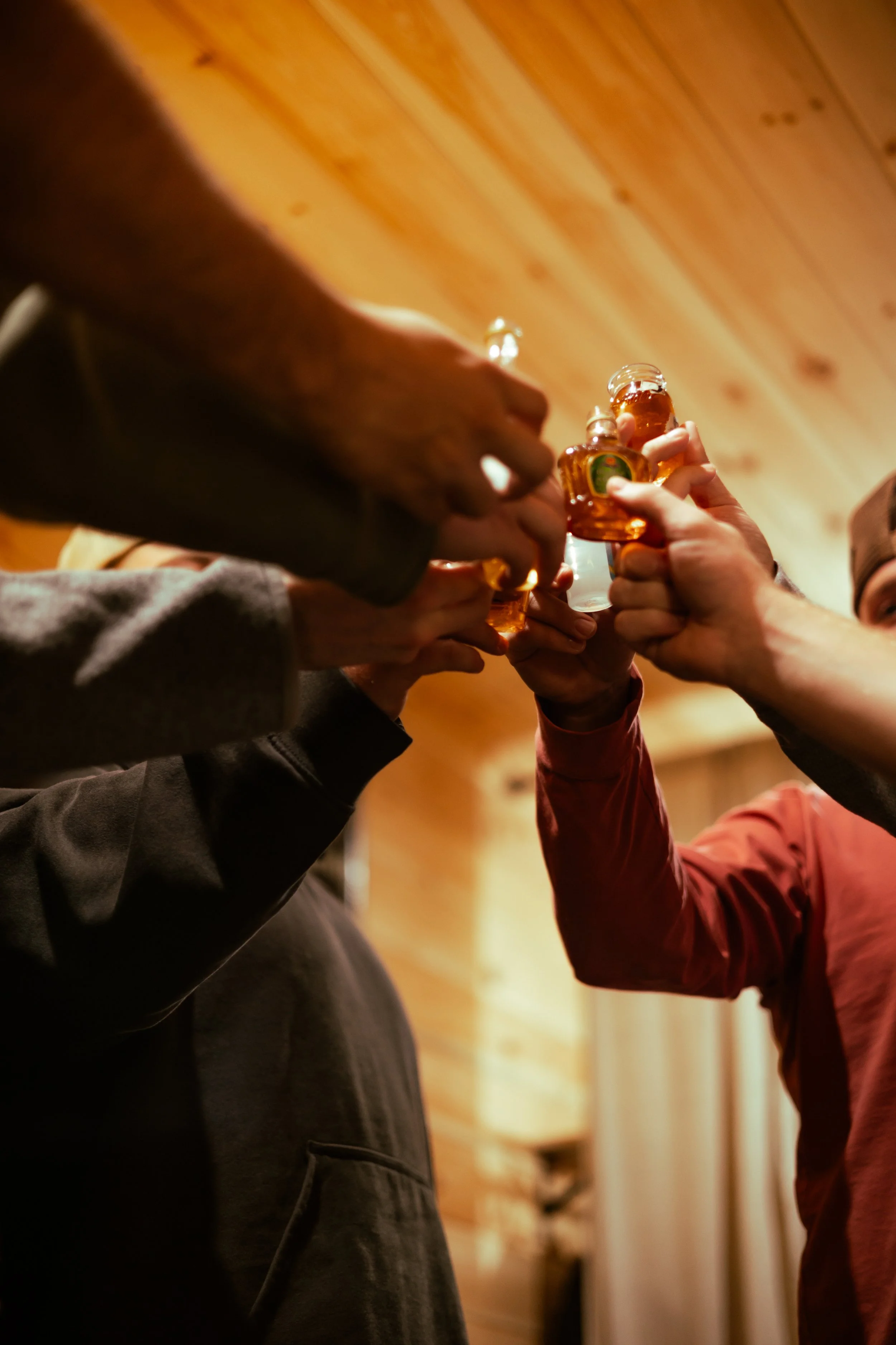 A group of people raising small bottles in a toast inside a wooden-paneled room.