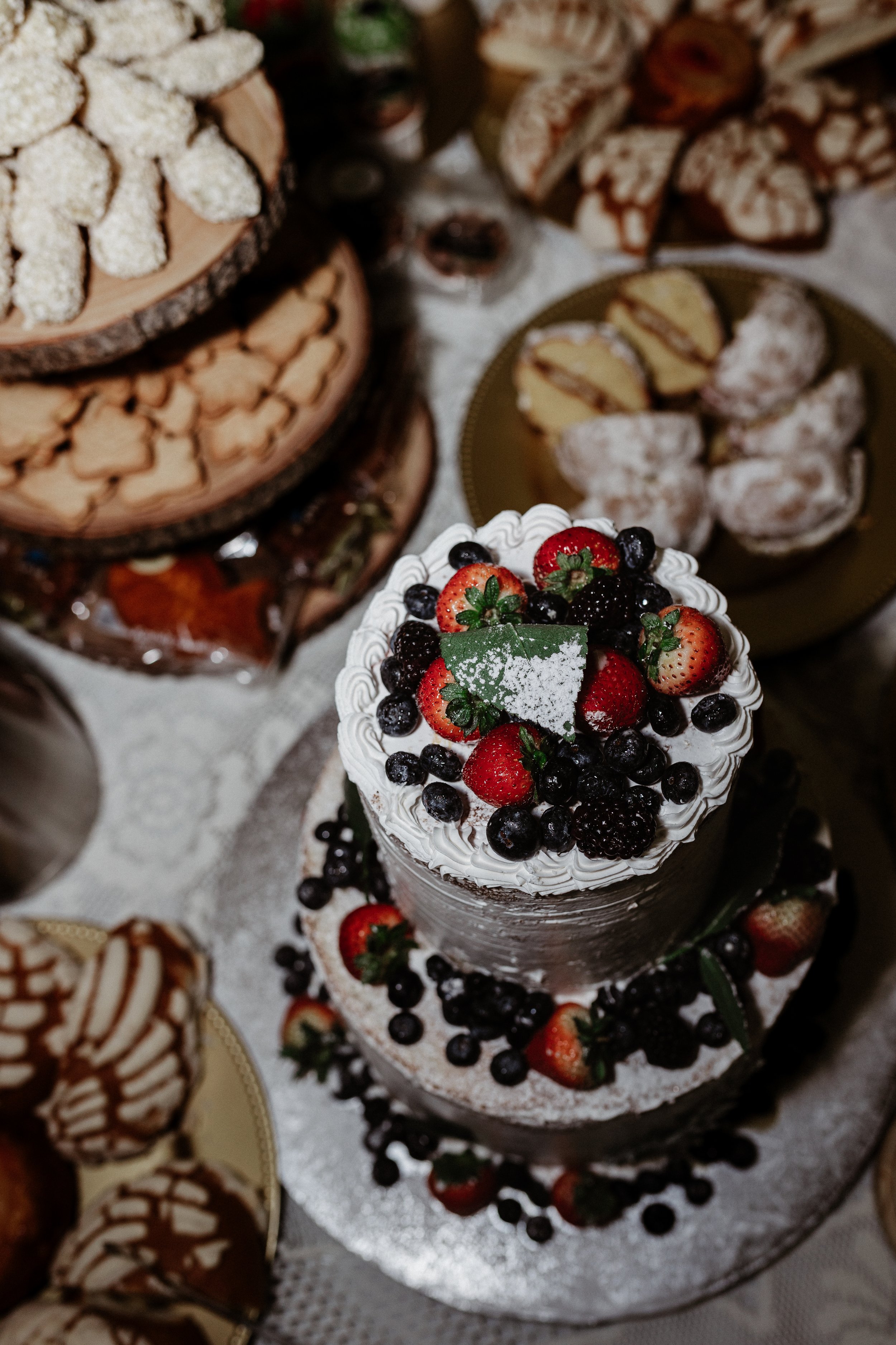 A layered cake decorated with strawberries, blueberries, blackberries, and a green leaf topper, topped with whipped cream and dusted with powdered sugar. Wedding Photographer in Birmingham, AL specializing in editorial style photography