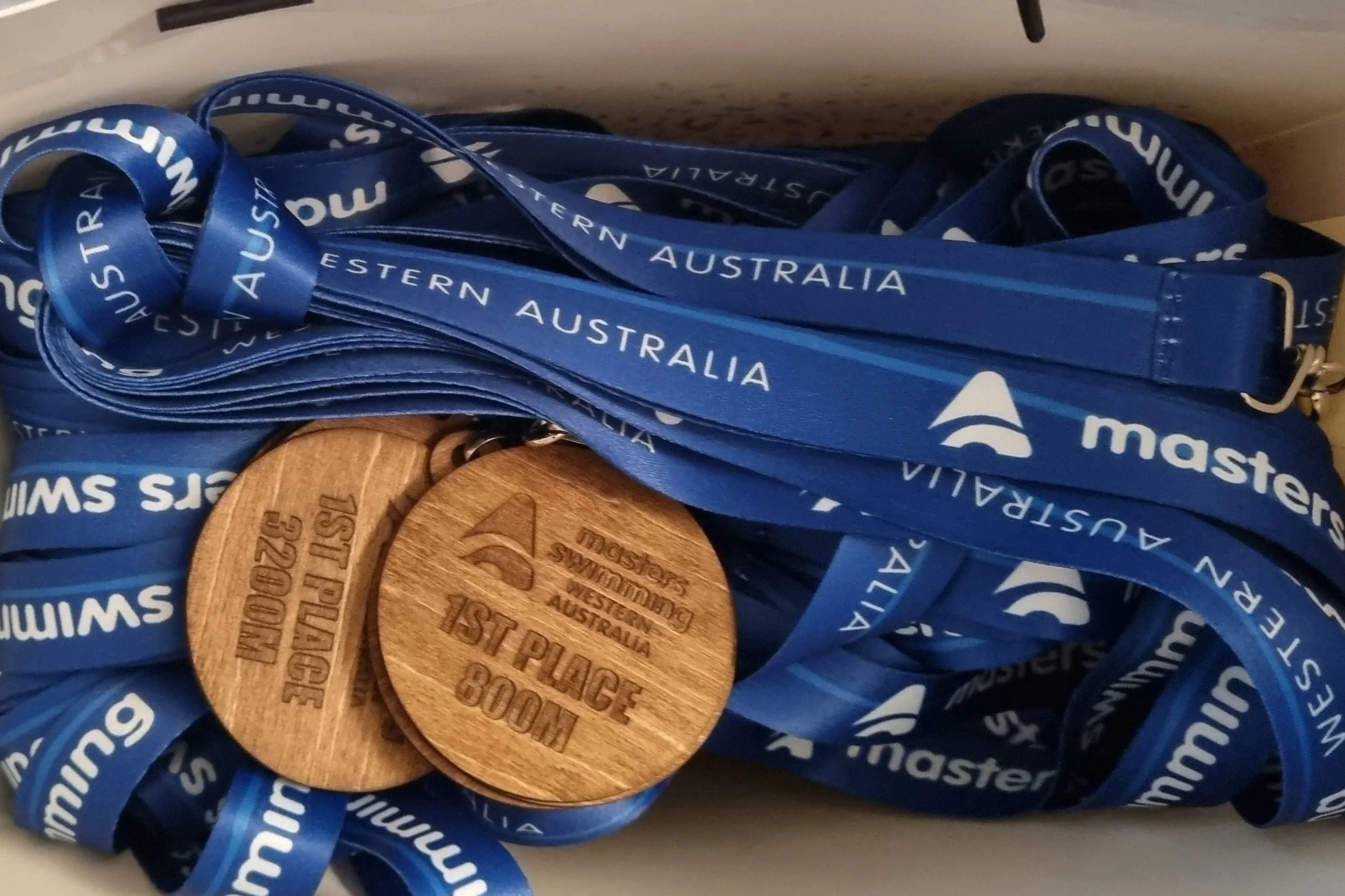 Swimming medals and ribbons from Masters Swimming Western Australia, including two wooden medals with engraved text.