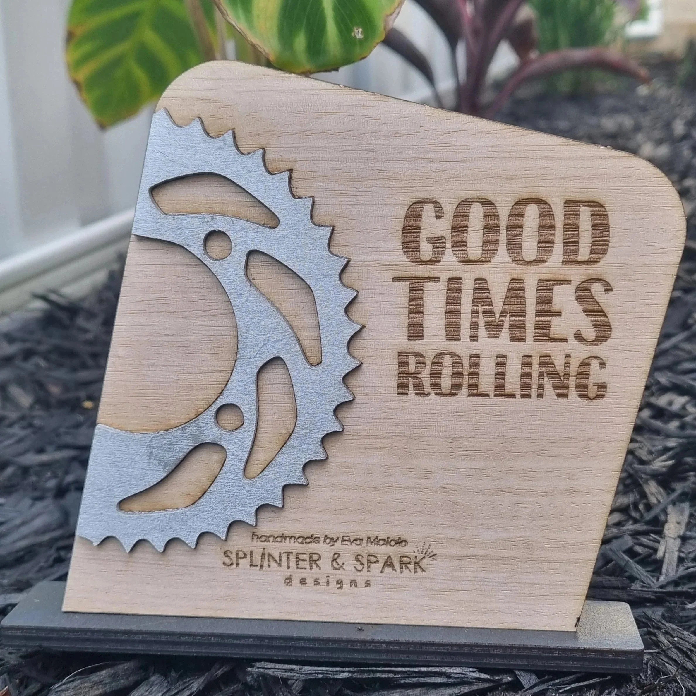 A wooden plaque with a metal bike gear and the words 'Good Times Rolling' engraved on it. The plaque also has the text 'Handmade by Ed Moido' and 'Splinter & Spark Designs' at the bottom.