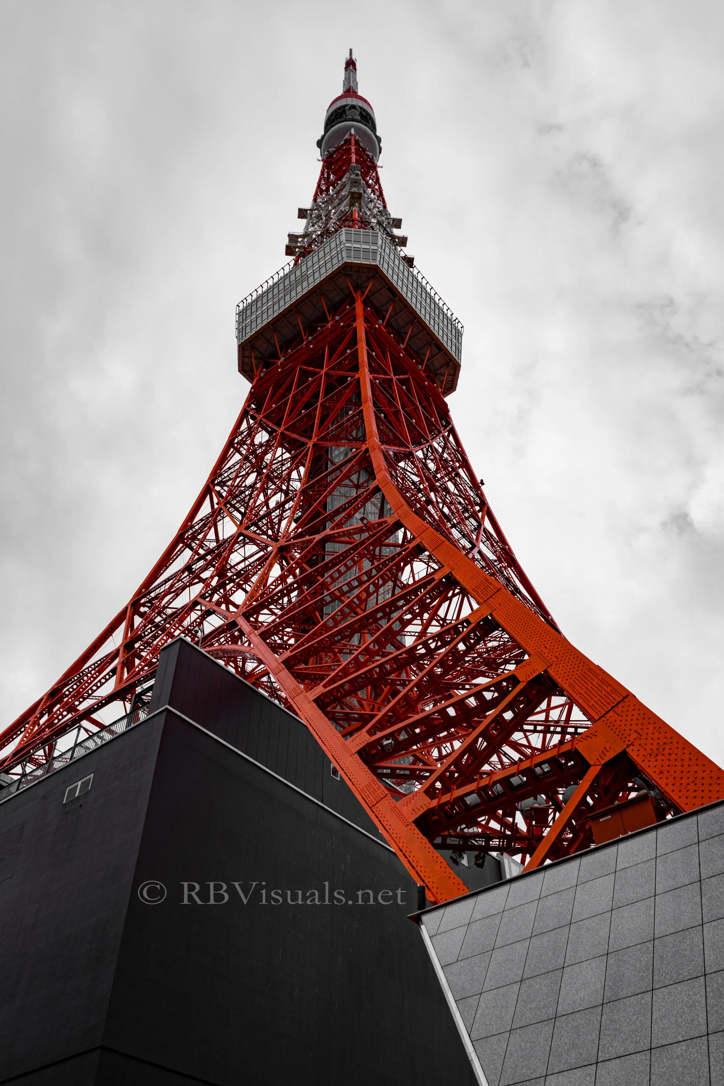 Low-angle view of Tokyo Tower against cloudy sky, showing red and white lattice structure and observation deck.
