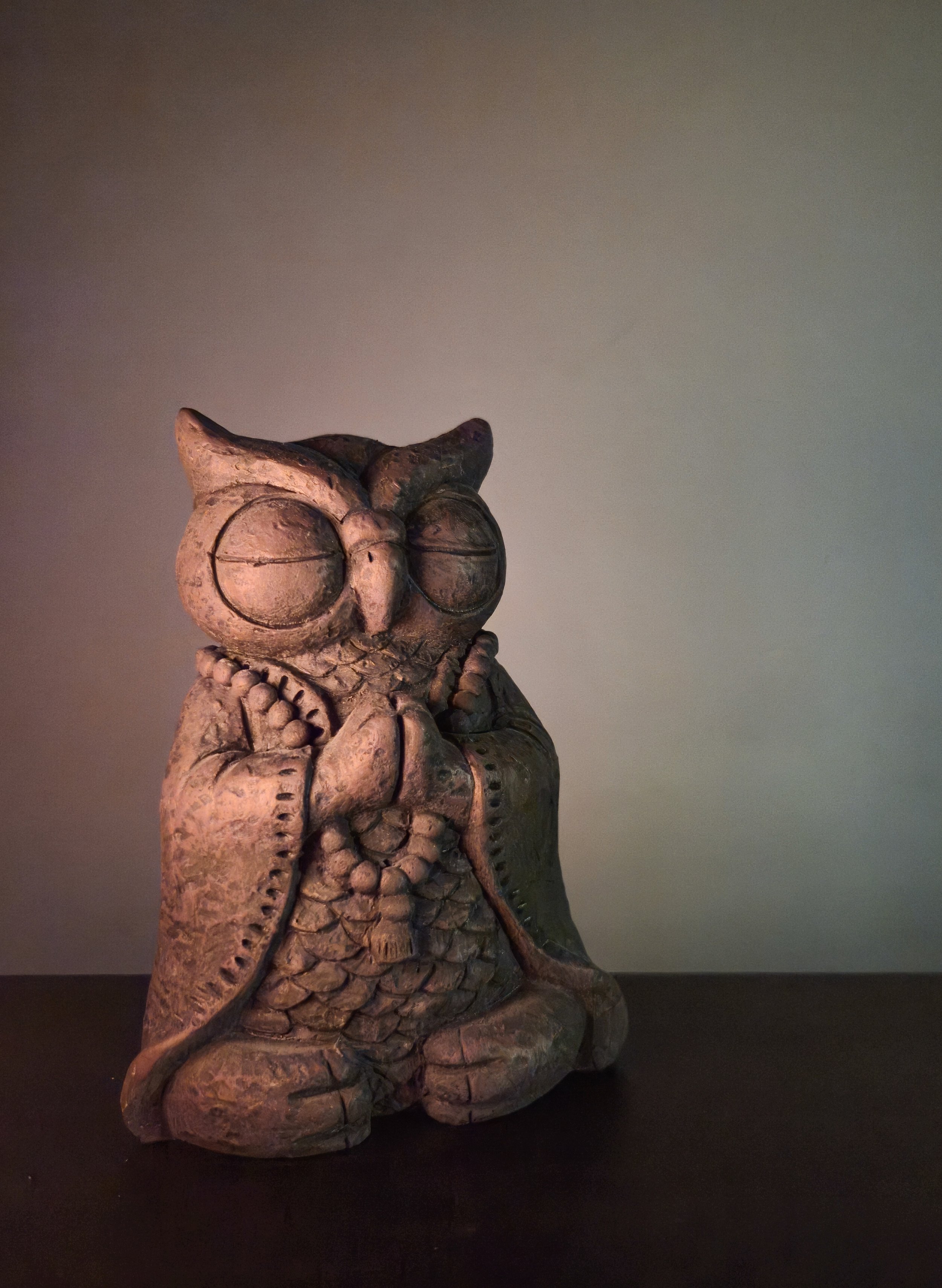 A ceramic figurine of an praying owl with closed eyes, wearing a robe, and holding a string of prayer beads, sitting on a flat surface against a plain background.